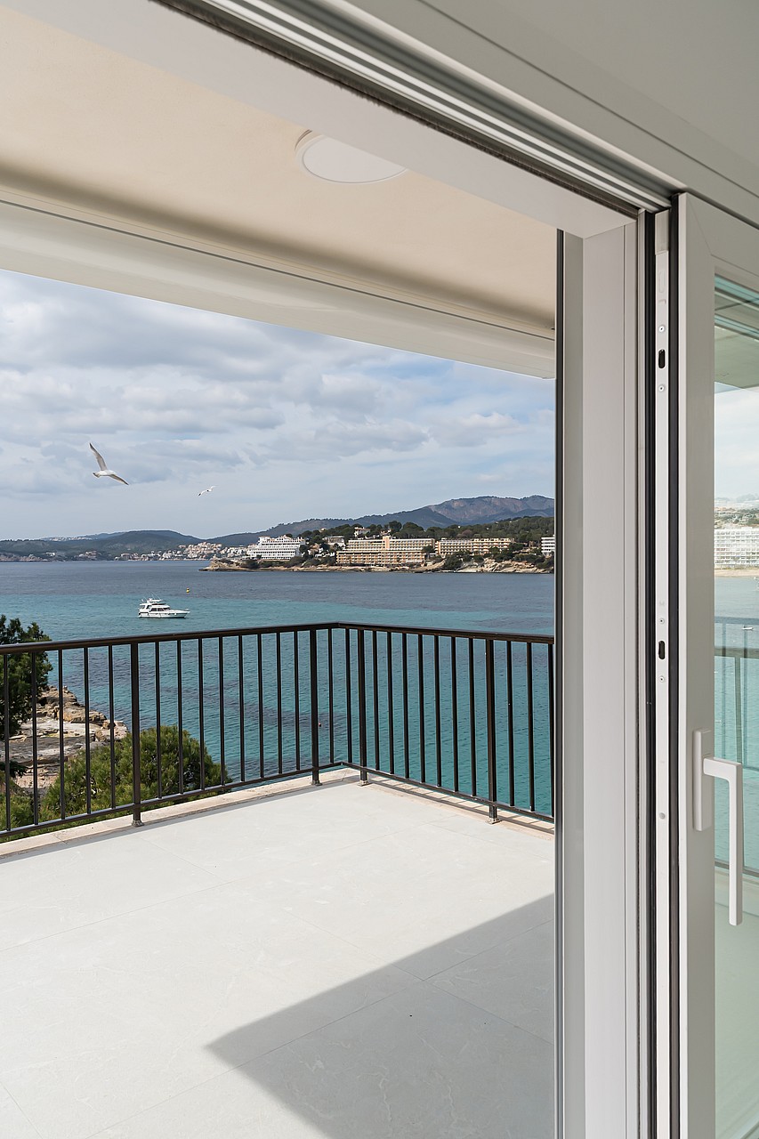 A white tiled terrace with dark metal railings overlooking a clear turquoise bay and distant mountains.
