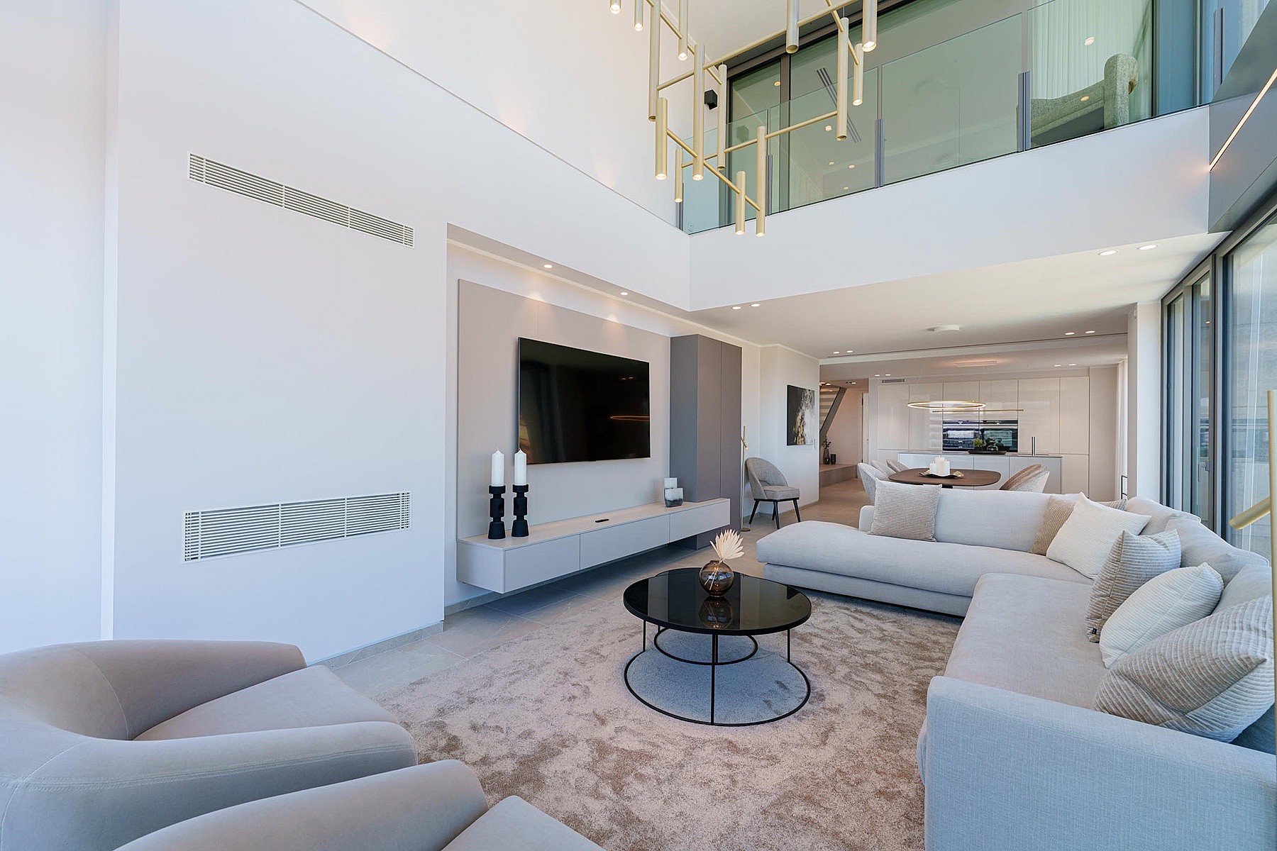 Salón moderno de planta abierta y doble altura con sofá blanco, mesas de cristal y pared equipada para televisión.