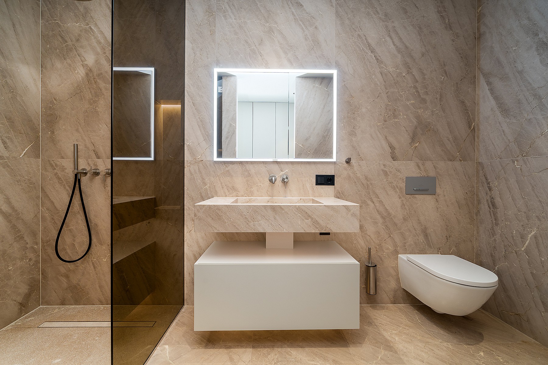 A modern bathroom featuring beige stone wall cladding, a floating vanity unit, a wall-mounted toilet, and a glass-enclosed shower.