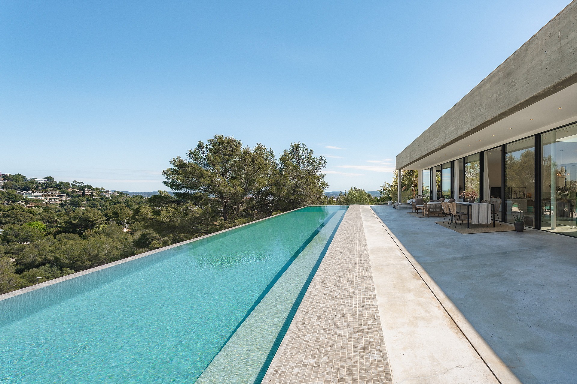A long infinity lap pool runs alongside a minimalist concrete terrace with views of green Mediterranean hills.