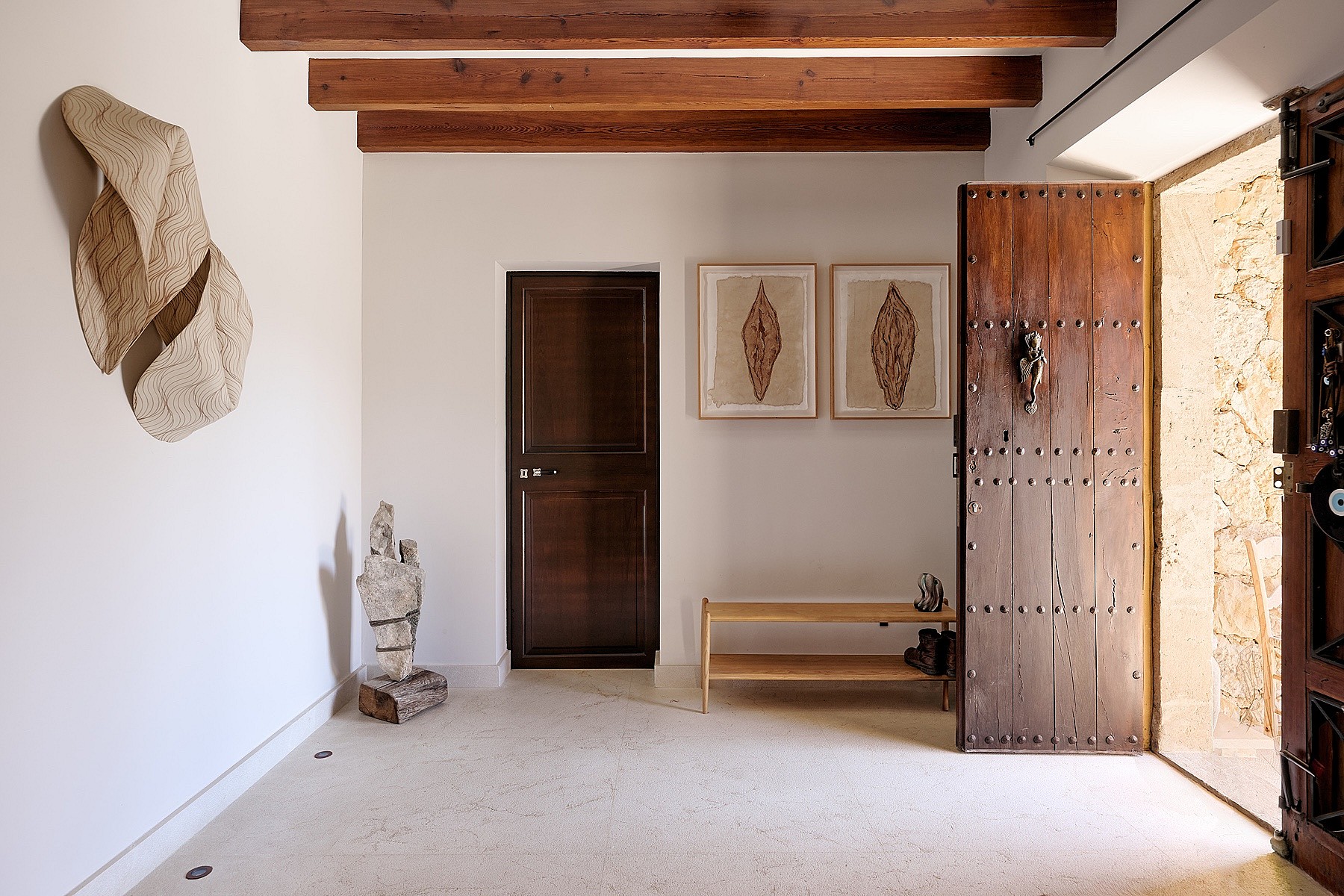 Entry foyer of a finca featuring white plastered walls, heavy dark wooden ceiling beams, and a large rustic timber door.