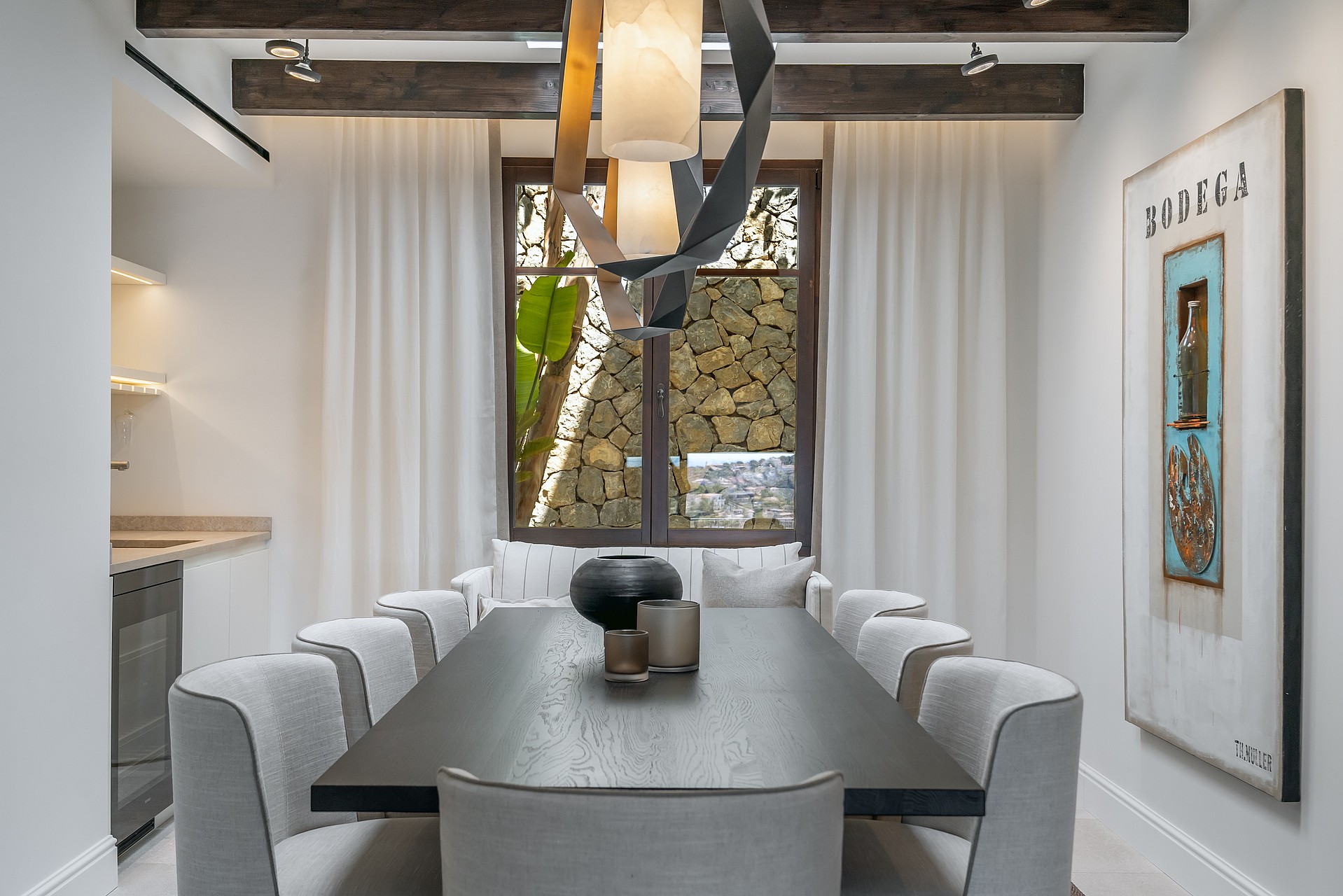 Dining area with a dark wood table, grey chairs, exposed ceiling beams, and a sculptural light fixture.