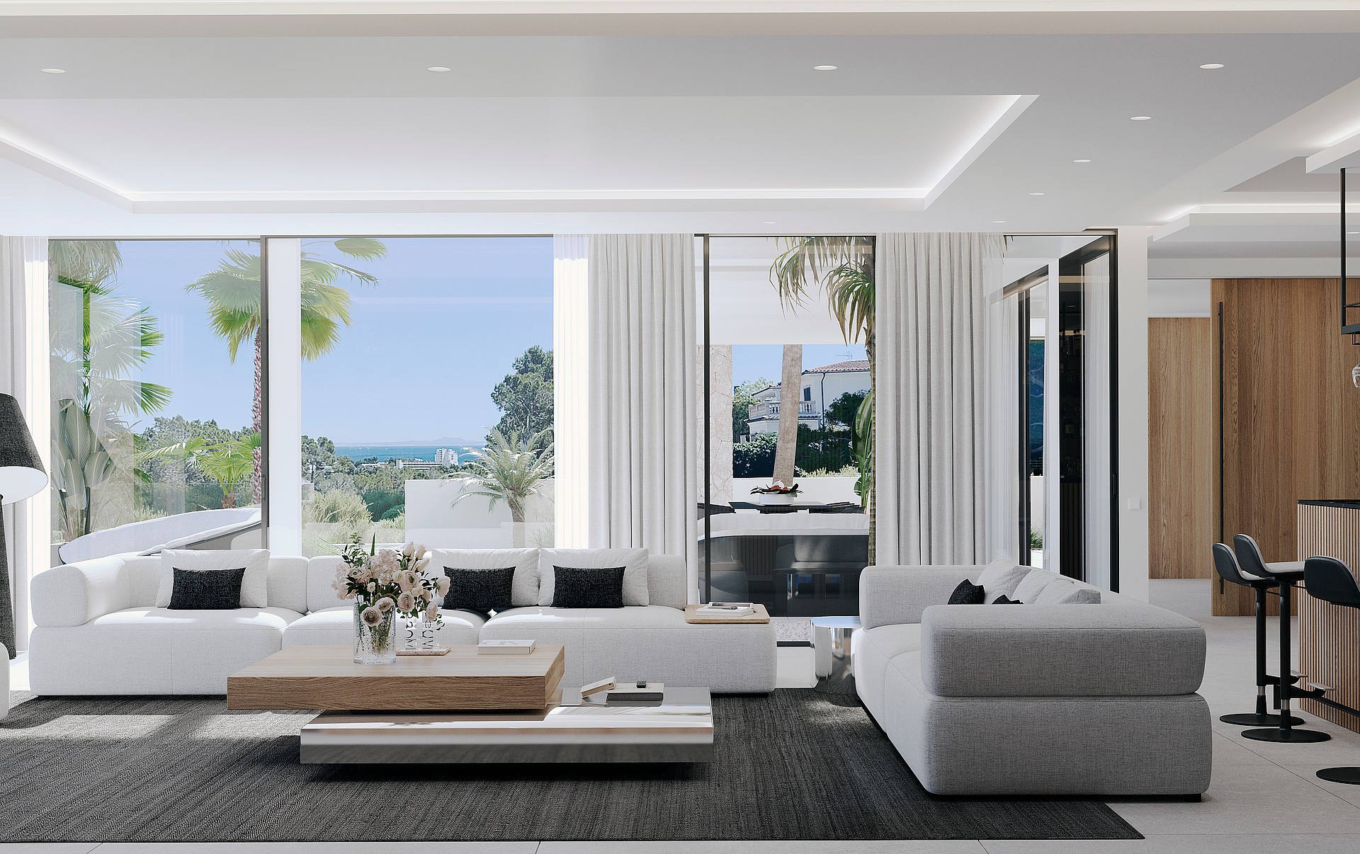 Modern open living room featuring white sofas, a light wood coffee table, dark area rug, and floor-to-ceiling sliding glass doors opening to a covered terrace with coastal views.