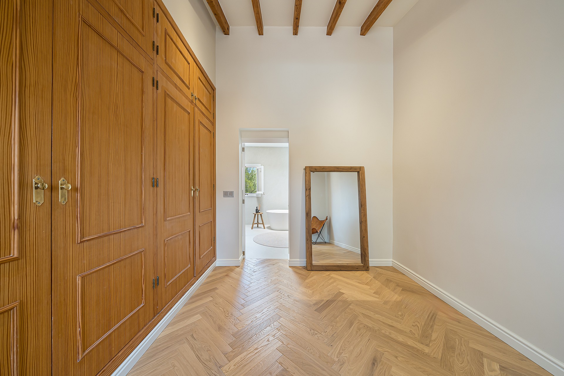 Dressing area with floor-to-ceiling wood wardrobes and herringbone parquet floors leading to an ensuite bathroom.
