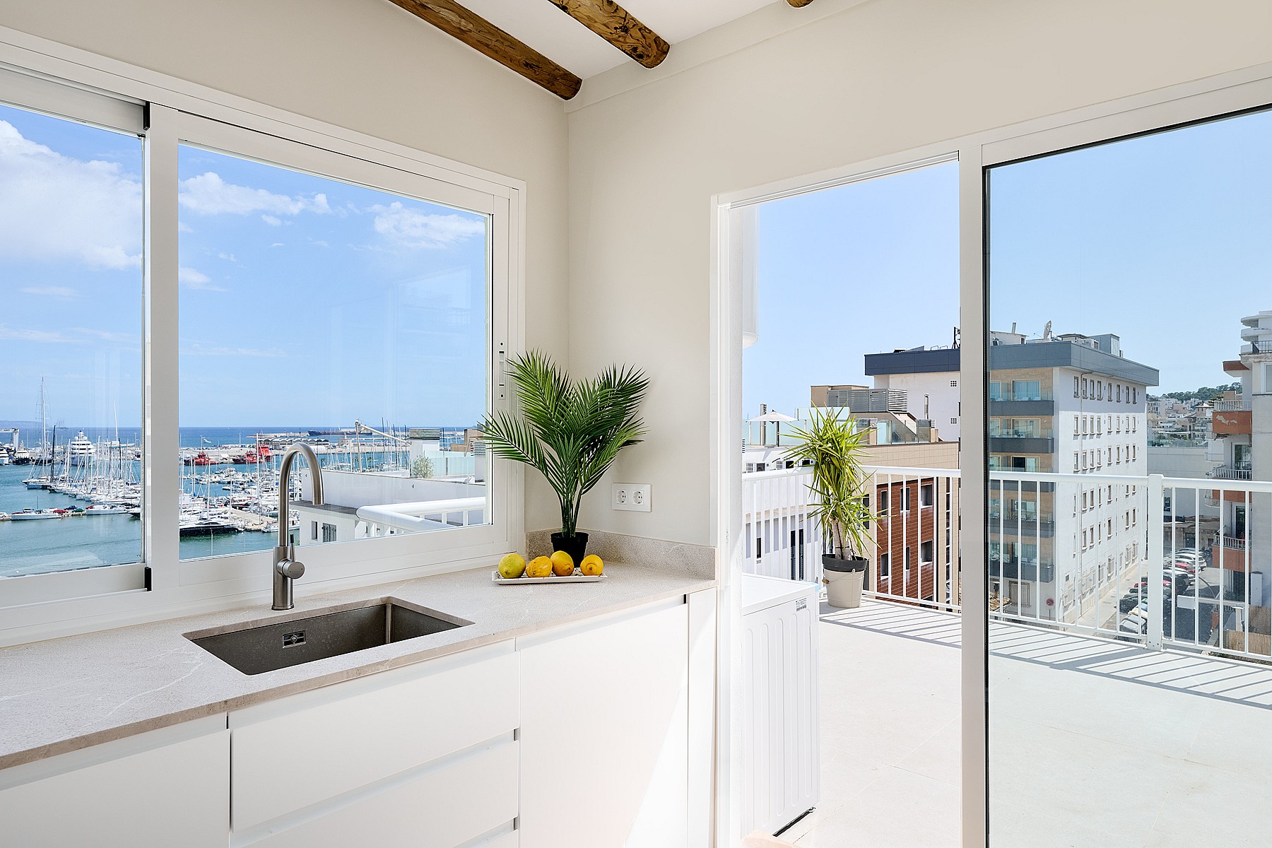 Modern kitchen corner with white cabinets and stone countertop, featuring large sliding glass doors opening to a balcony.