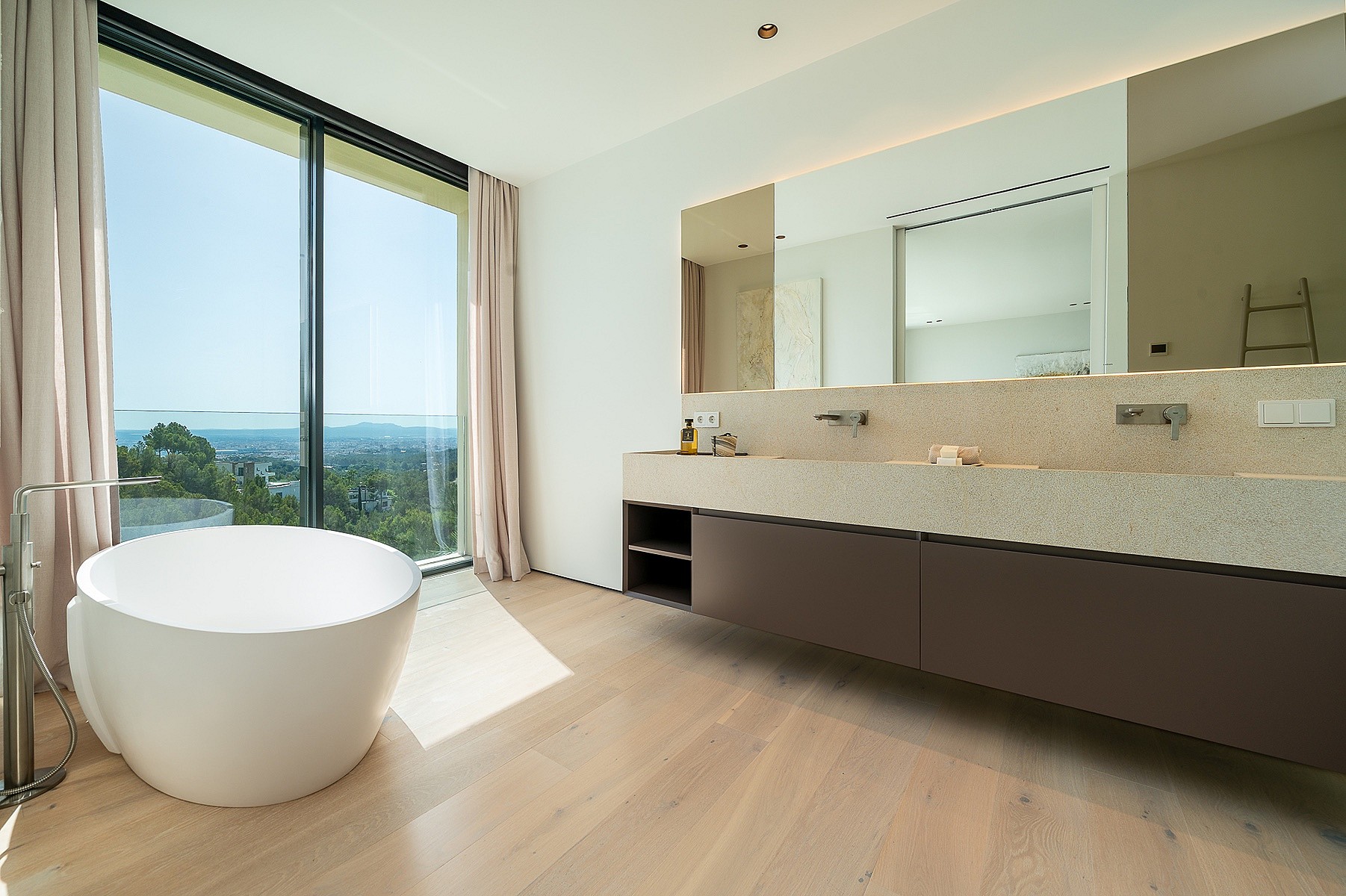 Modern bathroom featuring a white freestanding bathtub positioned beside a large floor-to-ceiling window overlooking the sea.