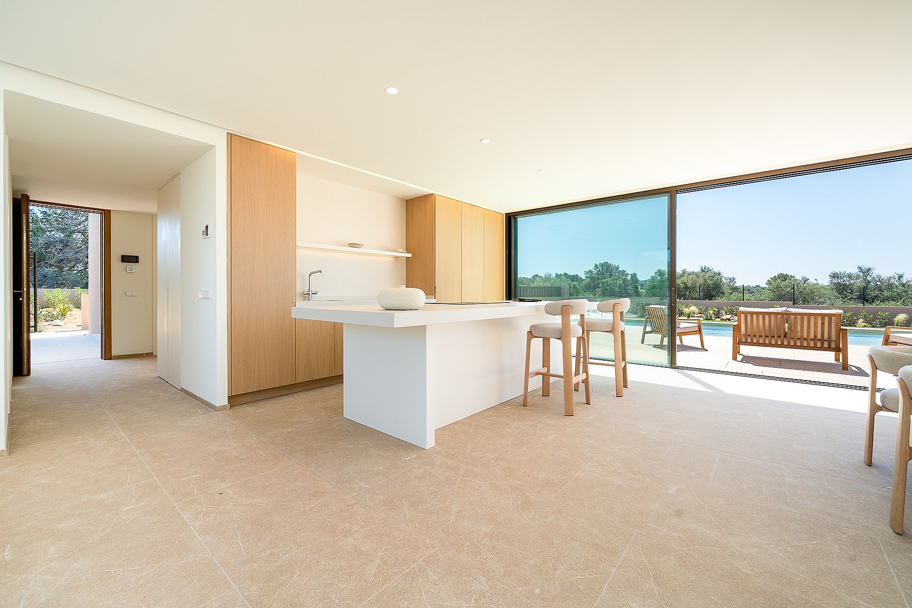 Modern open-plan kitchen with white island, light wood cabinetry, and floor-to-ceiling sliding glass doors opening to a terrace.