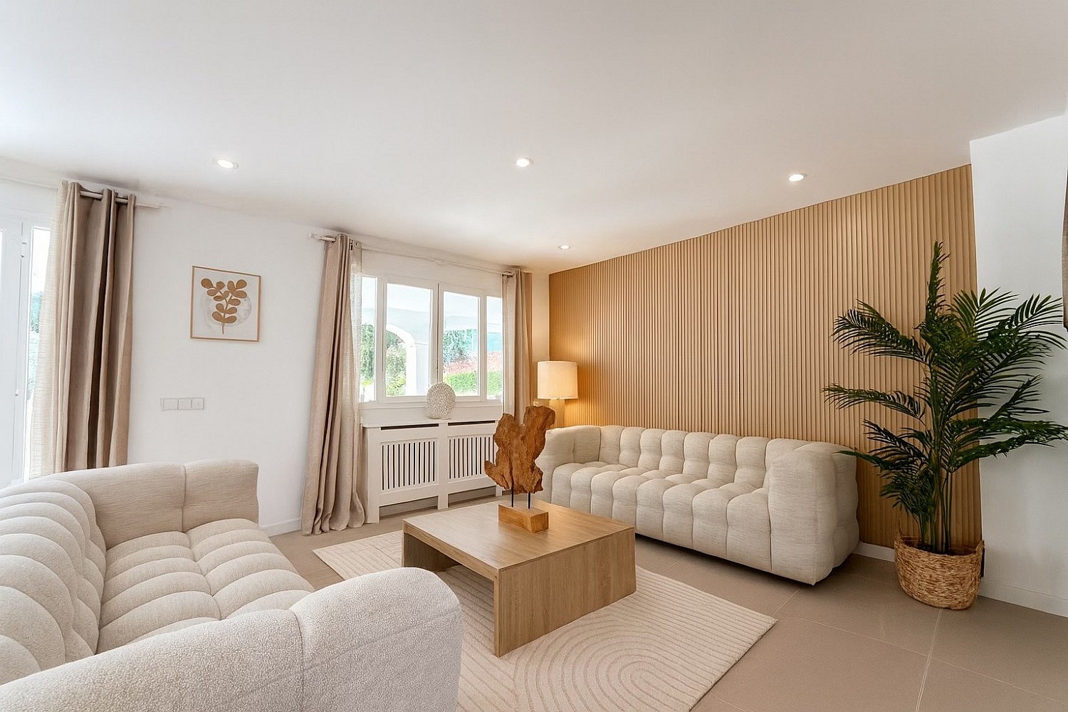 Living room with two cream bouclé sofas, wooden slat feature wall, low oak coffee table and tiled flooring