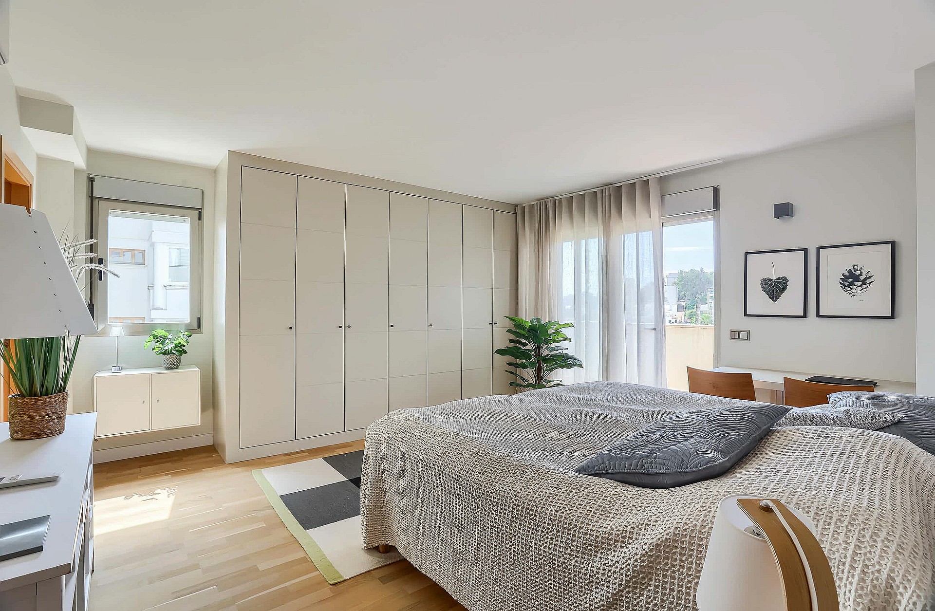 A modern bedroom with light wood flooring, a textured bedspread, and a large white built-in wardrobe with floor-to-ceiling doors.