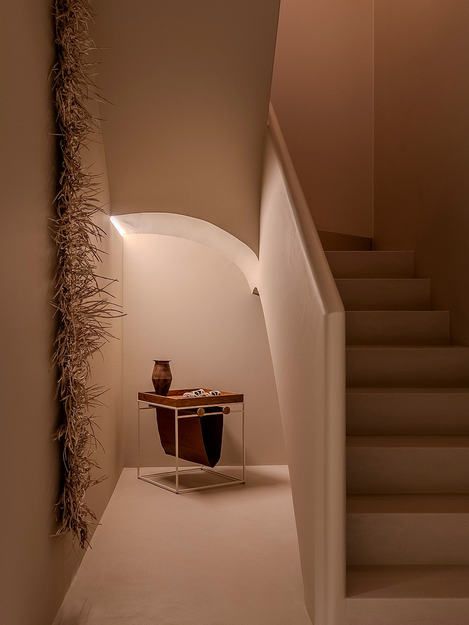A minimalist white staircase with smooth plastered walls, an integrated handrail, and soft warm recessed lighting.
