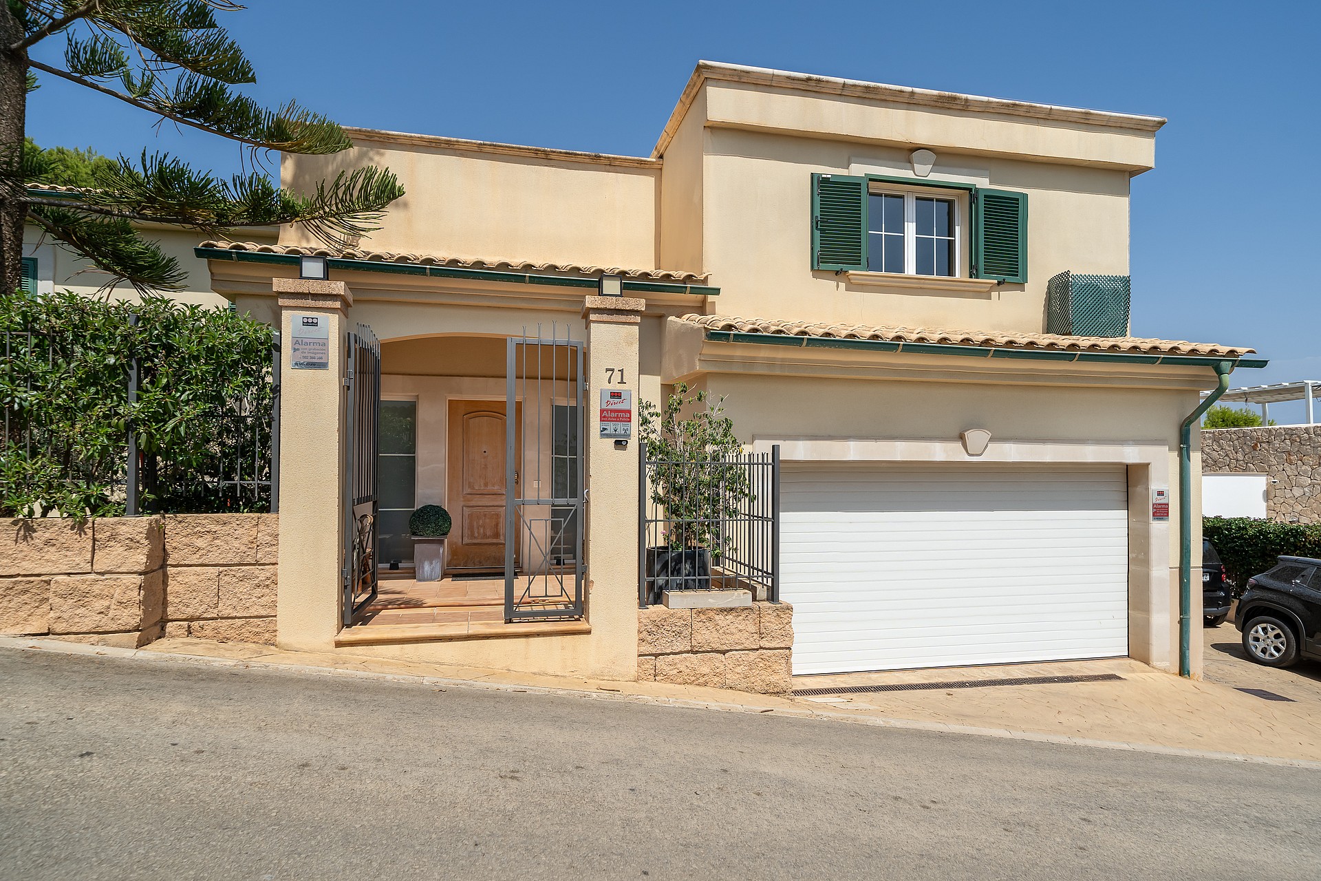 Exterior street-level view of a two-story villa featuring a pale rendered facade, green shutters, a private garage, and a gated entrance with stone accents.