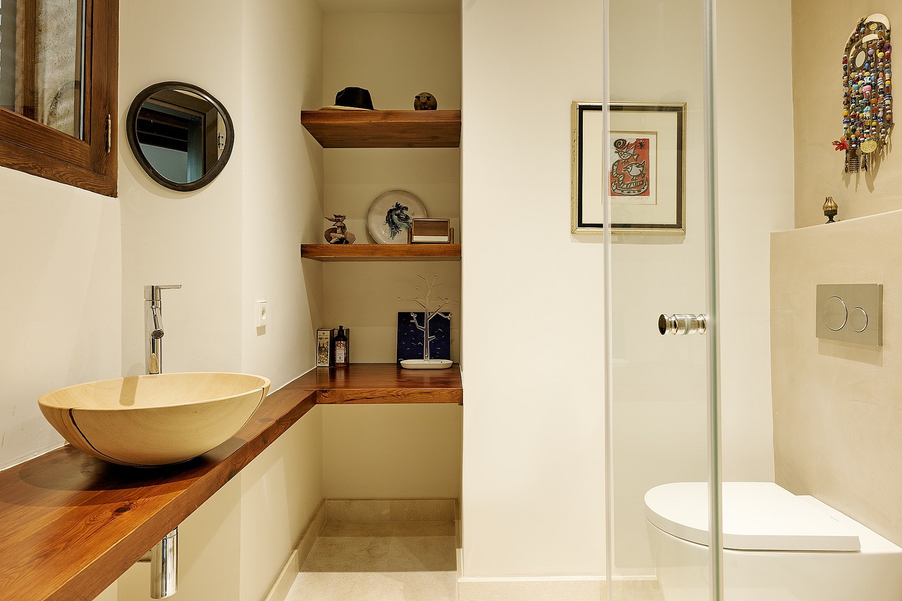 A modern bathroom featuring a circular stone vessel sink on a thick wooden vanity, open shelves, and a walk-in glass shower.