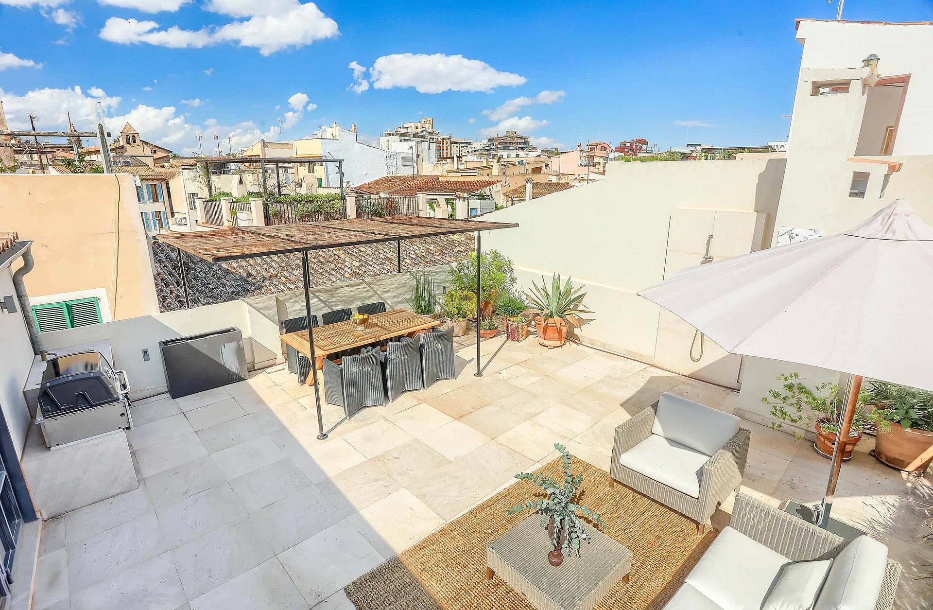 Aerial view of a paved rooftop terrace featuring outdoor dining furniture and seating area, overlooking the Old Town rooftops.
