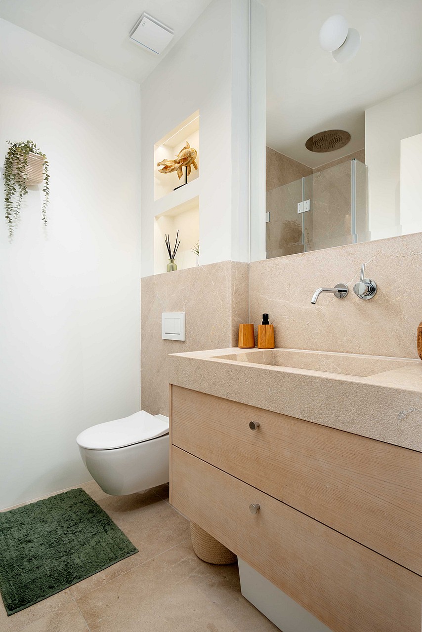 A modern guest bathroom featuring a wall-hung toilet, a vanity with natural stone surfaces, and recessed shelving.