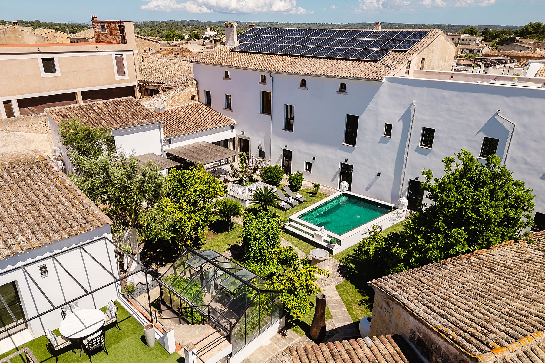 Aerial view of a Mediterranean townhouse central courtyard featuring a small swimming pool, surrounding gardens, and tiled roofs.