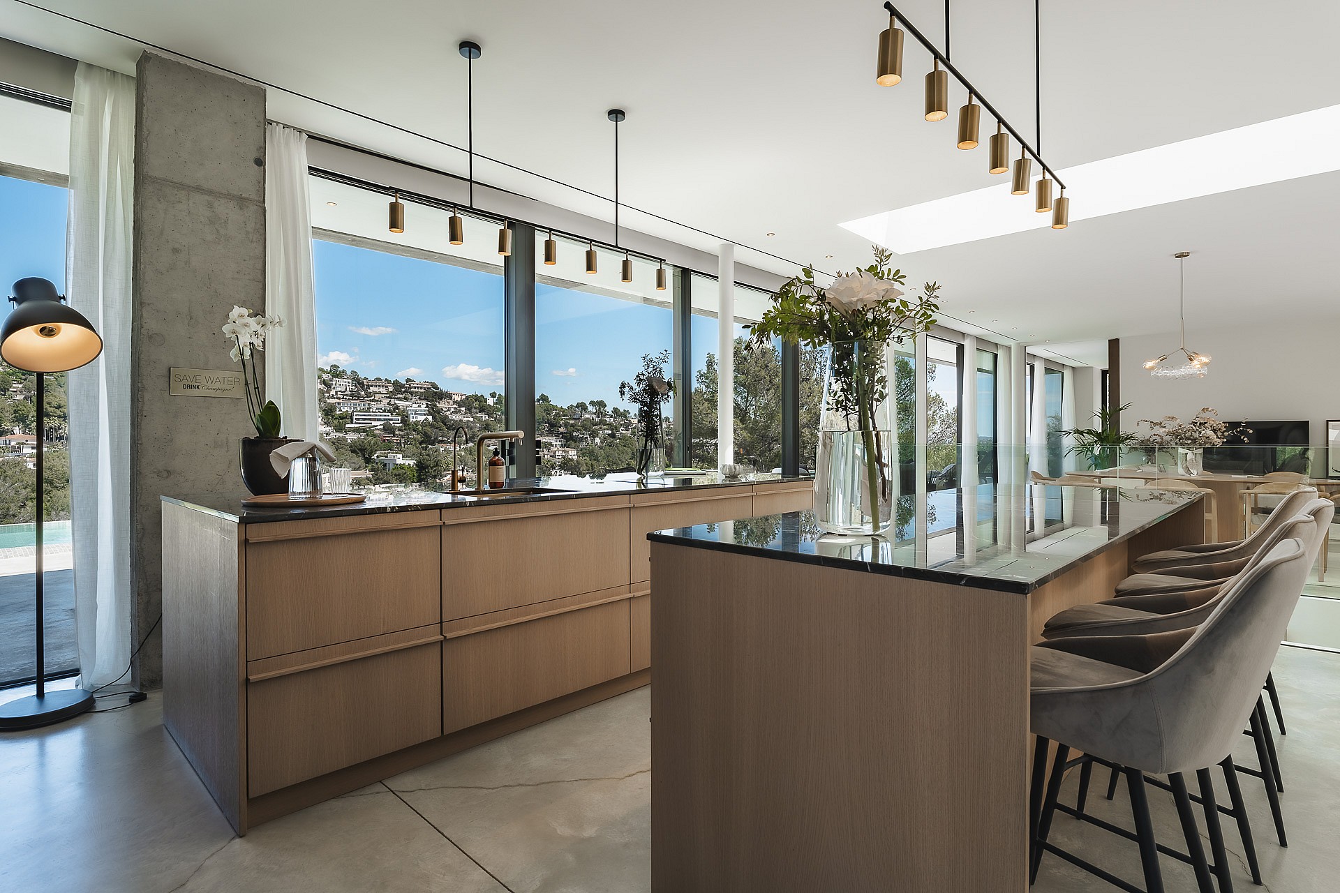 Contemporary kitchen featuring a wooden island with bar seating, dark countertops, and windows overlooking green hills.