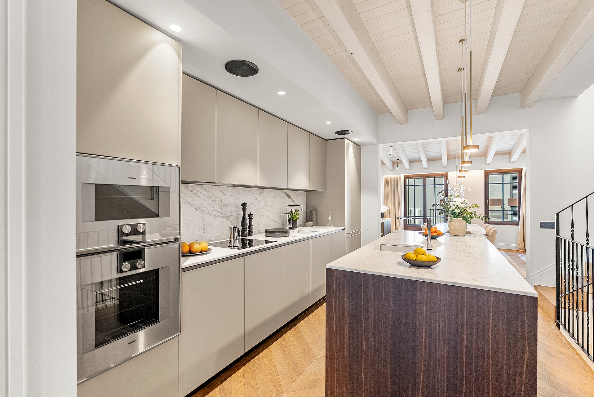 Modern kitchen featuring a dark wood island, marble countertops, white cabinetry, and herringbone oak flooring.