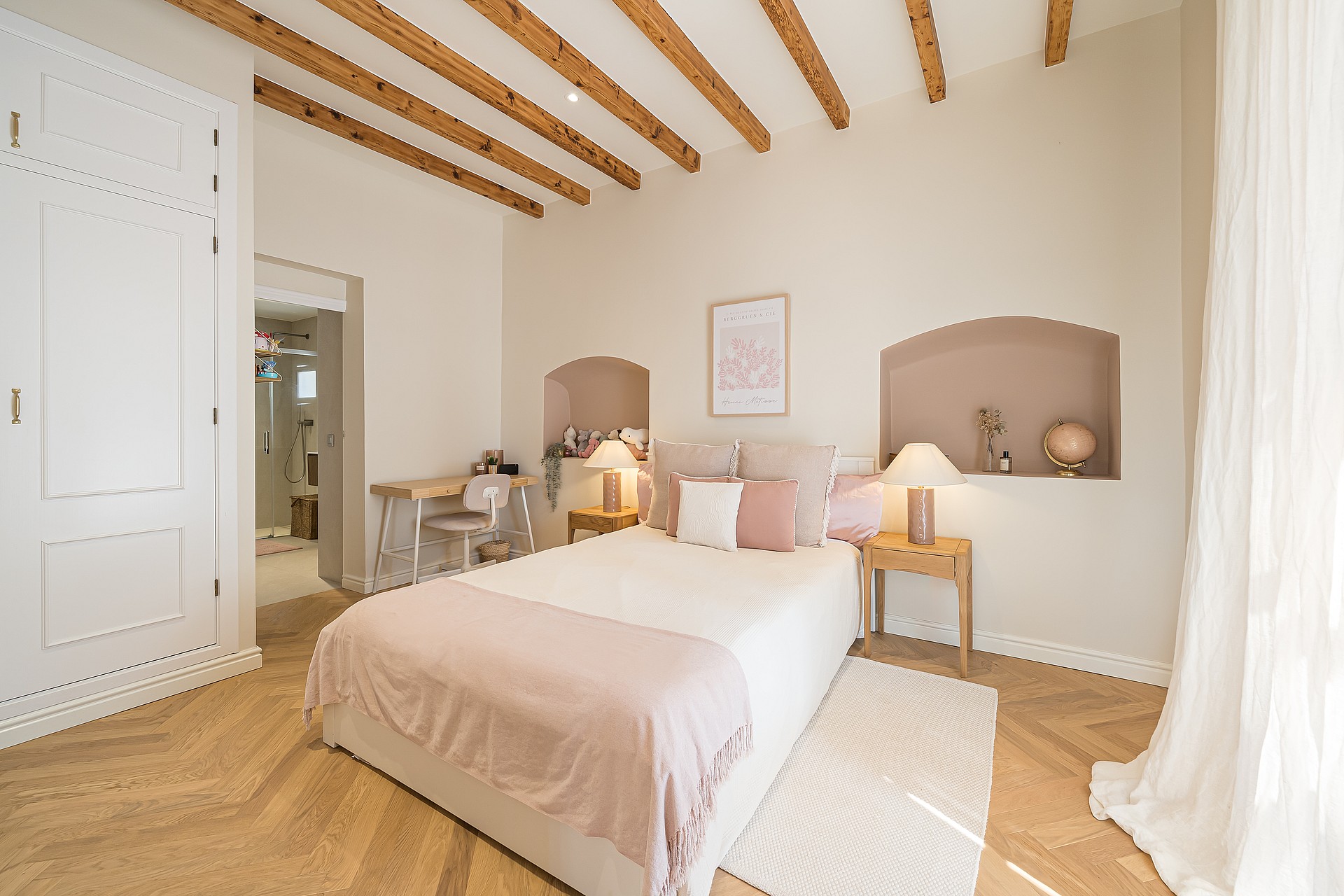 Bright bedroom featuring exposed ceiling beams, herringbone wood floors, and recessed wall arches above a double bed.