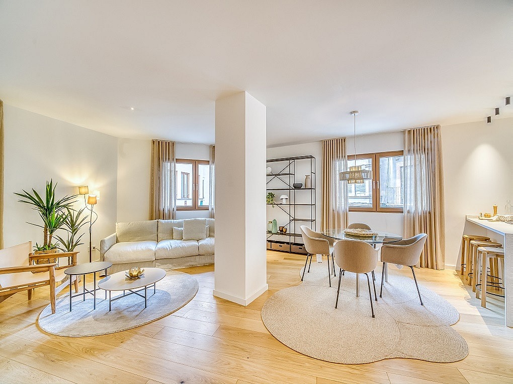 An open-plan living and dining room with oak floors, a central structural column, and neutral beige furniture.