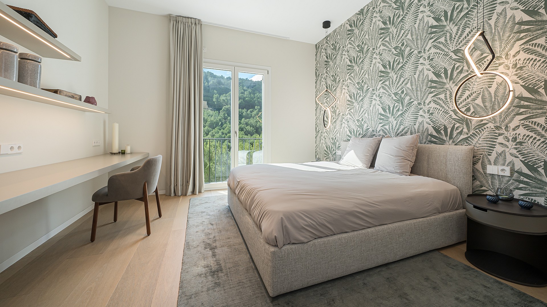 A modern bedroom featuring a patterned leaf-print wallpaper, a platform bed with grey bedding, and a built-in desk area.
