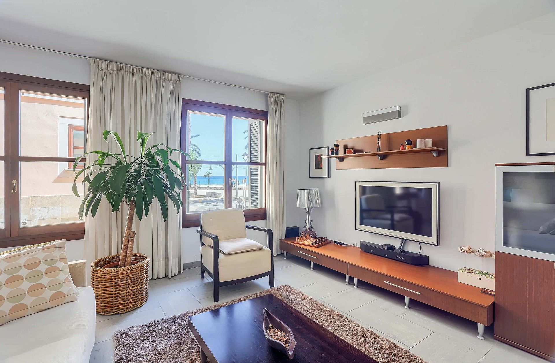 Living room with cream furniture, a wooden media console, potted plant, and windows framing a sea view in the Old Town.