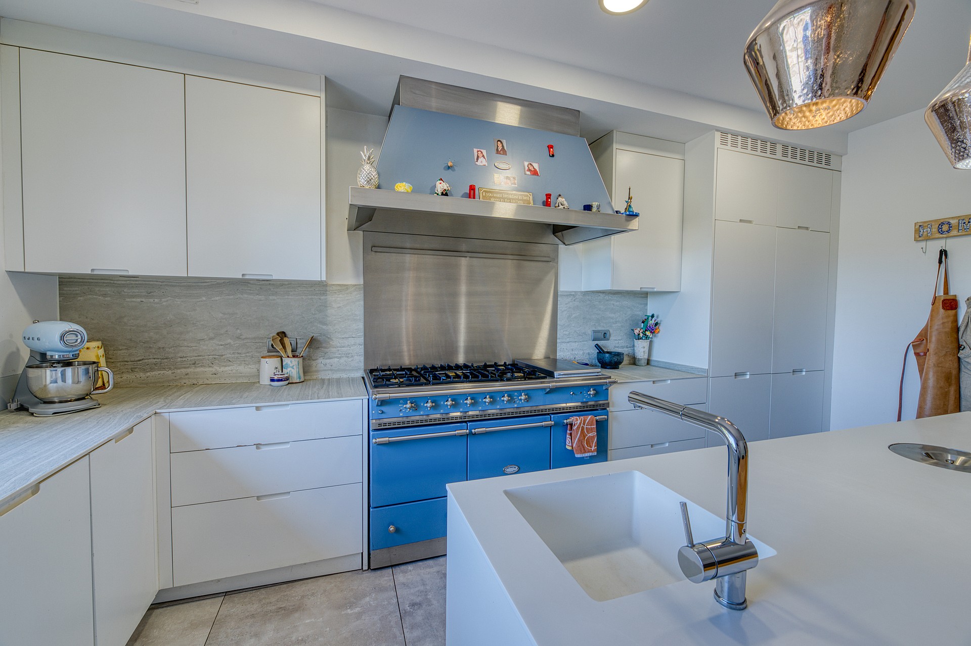 A modern kitchen featuring a bright blue range cooker, matching hood, white cabinetry, and a large central island with a sink.