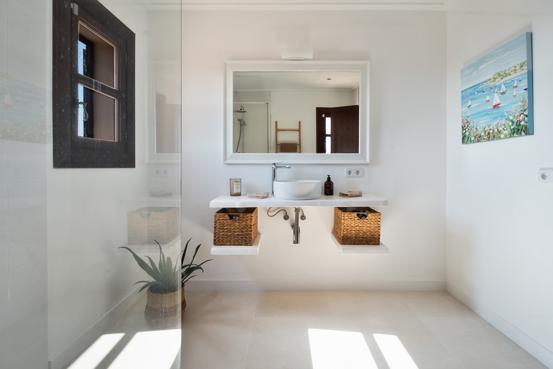 Baño minimalista con mueble blanco suspendido, cestas de mimbre, espejo rectangular y ducha de cristal.