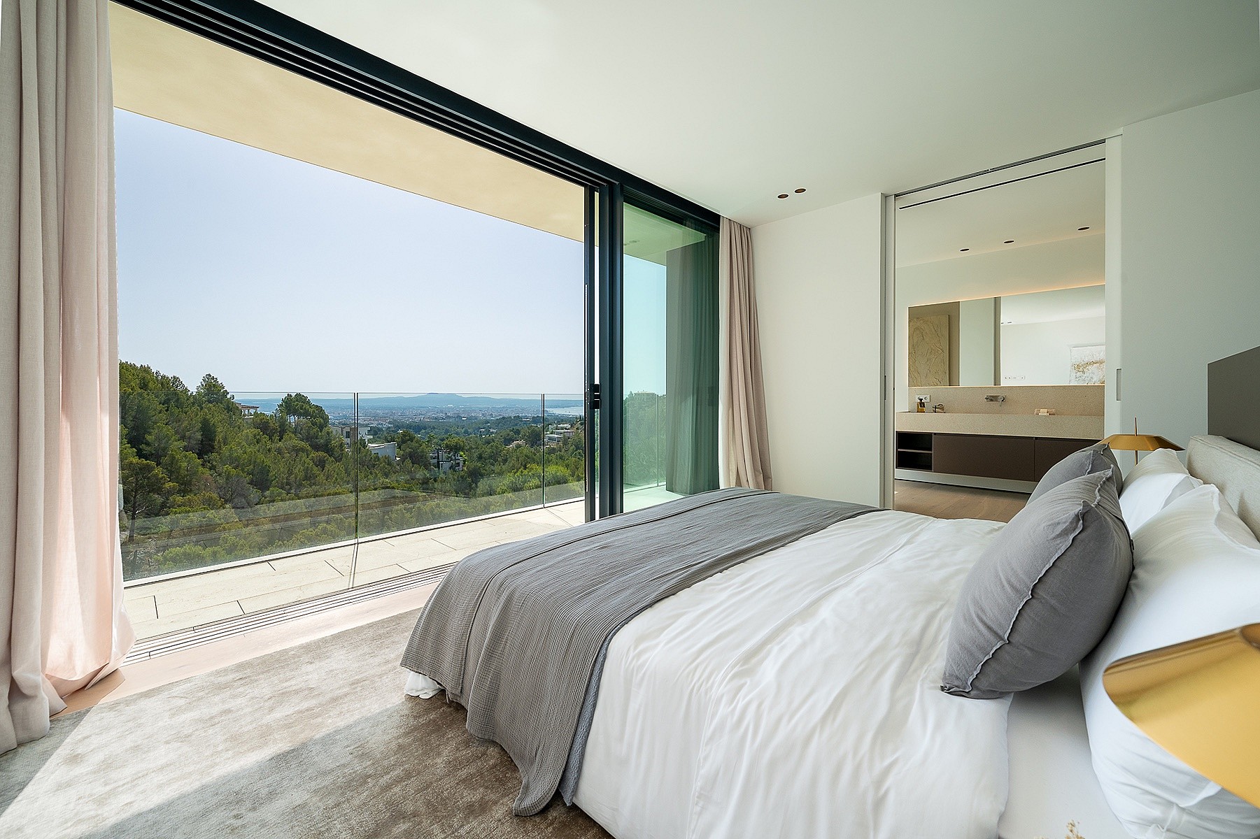 A modern master bedroom with a large bed, floor-to-ceiling sliding glass doors opening to a balcony with sea views.