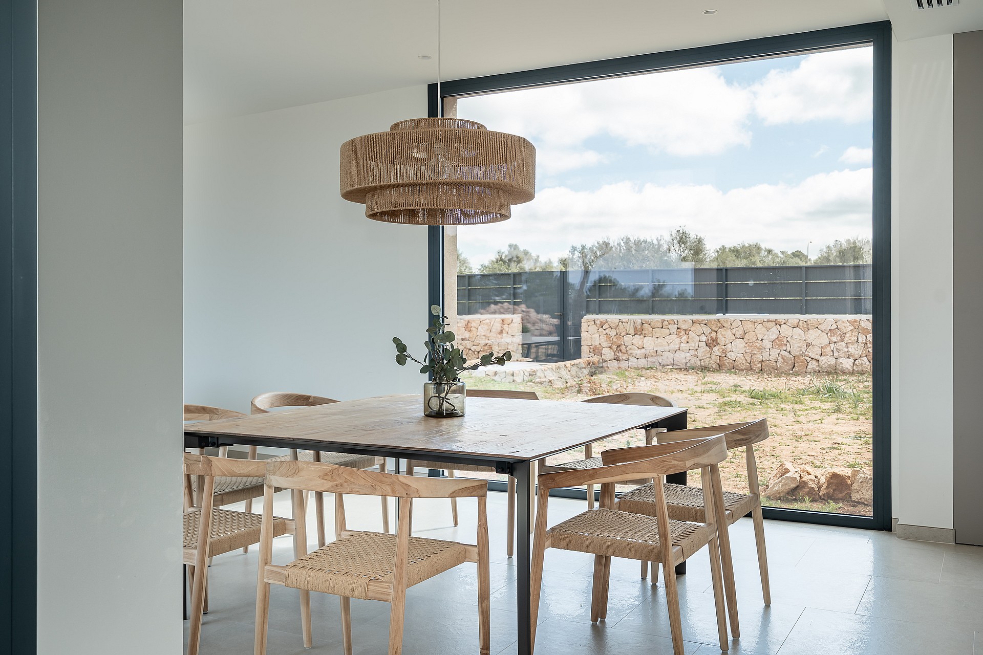 Dining area featuring a wooden table, woven chairs, and a large pendant light set against a window with mountain scenery.