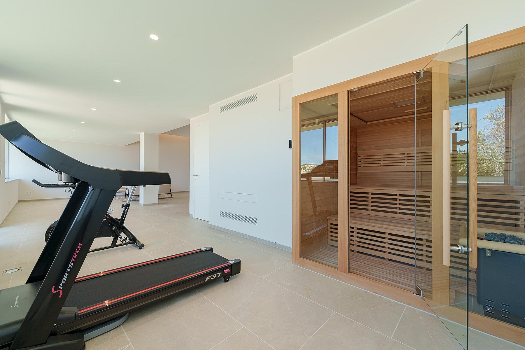 A modern home fitness room containing a treadmill and a glass-enclosed cedar wood sauna with tiered bench seating.
