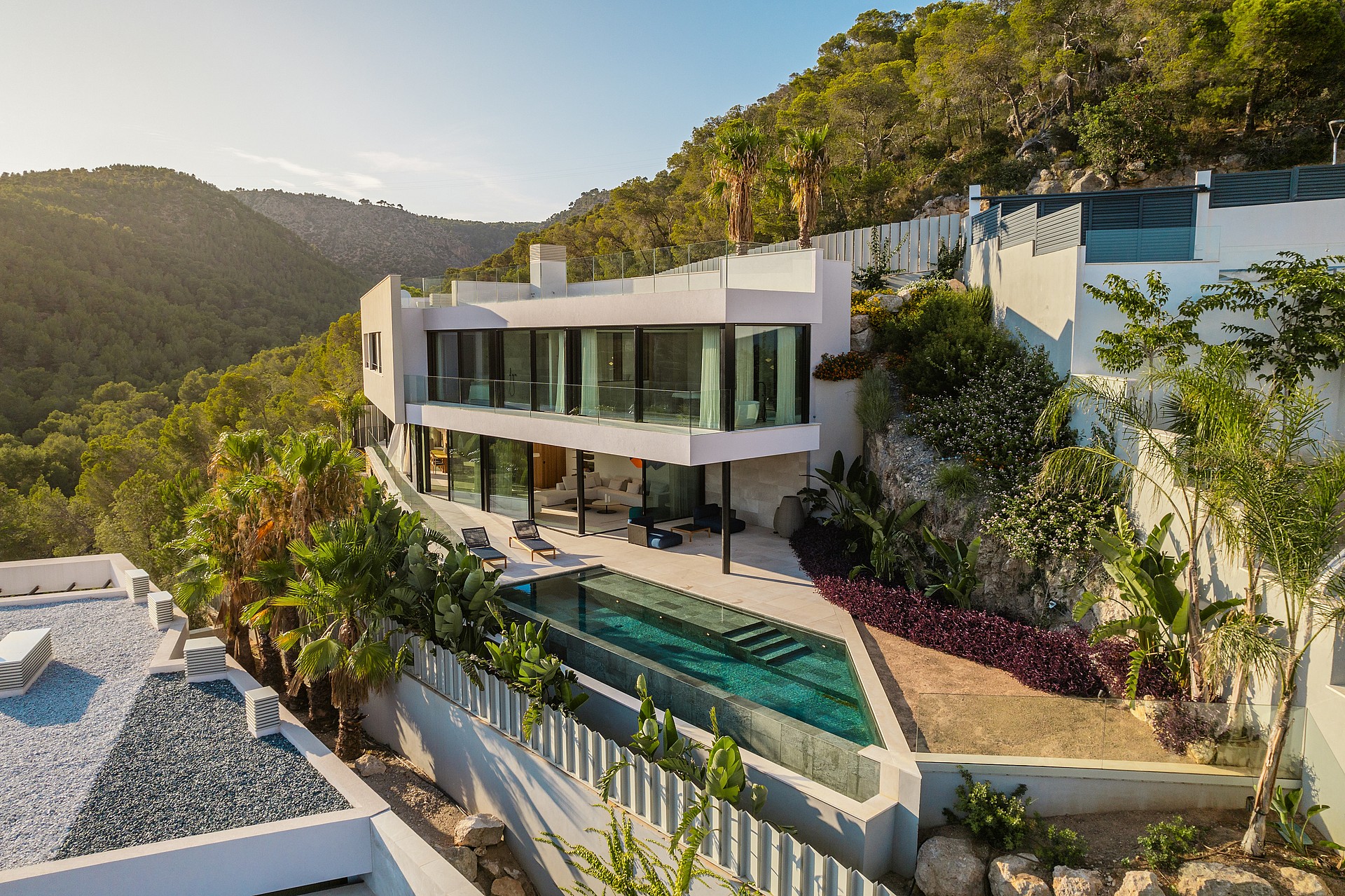 A contemporary white villa built into a hillside with floor-to-ceiling glass walls, a tiered terrace, and a private pool.