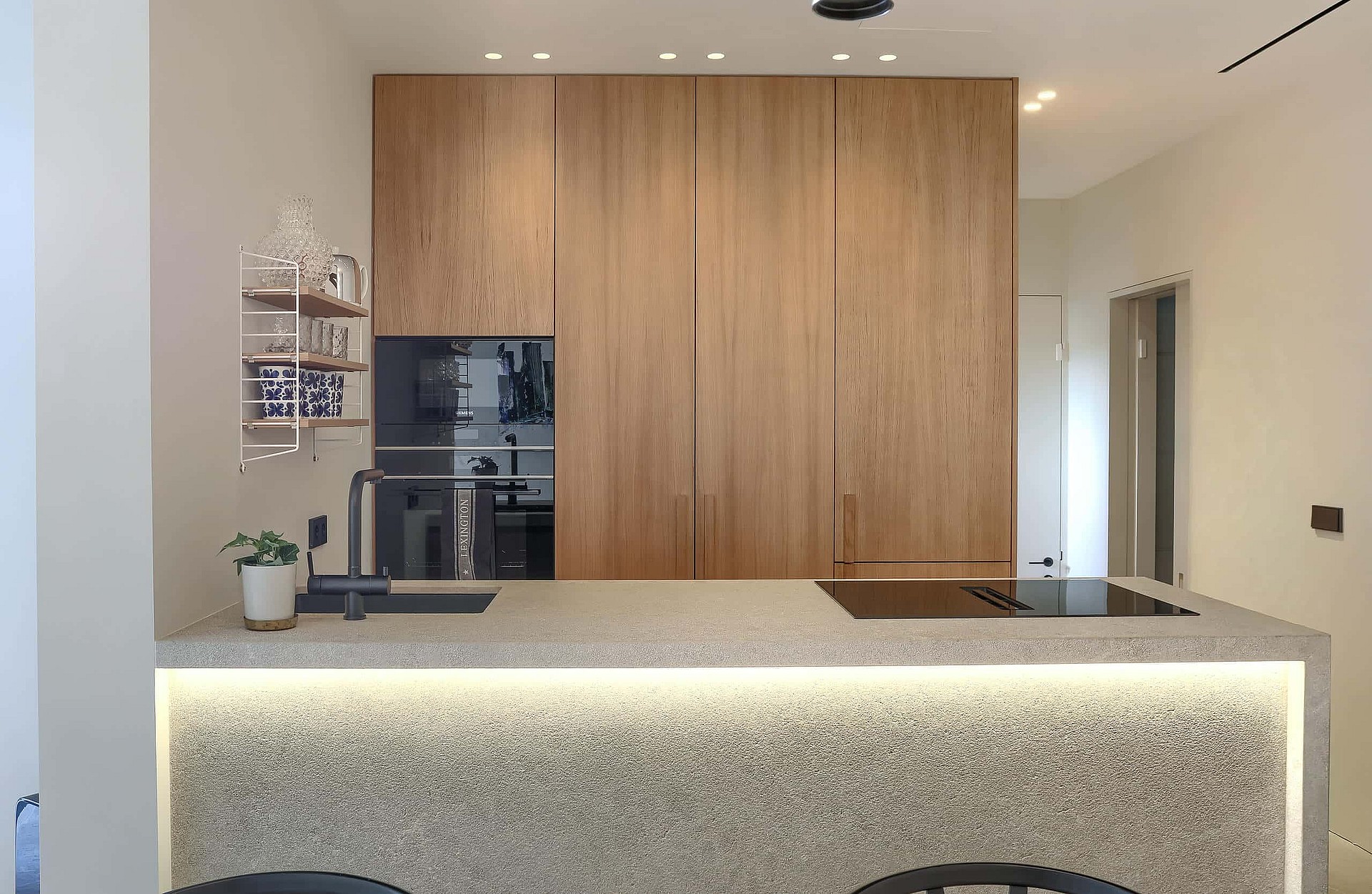 A modern kitchen island with a speckled terrazzo surface and under-counter LED lighting, paired with floor-to-ceiling wood cabinetry.