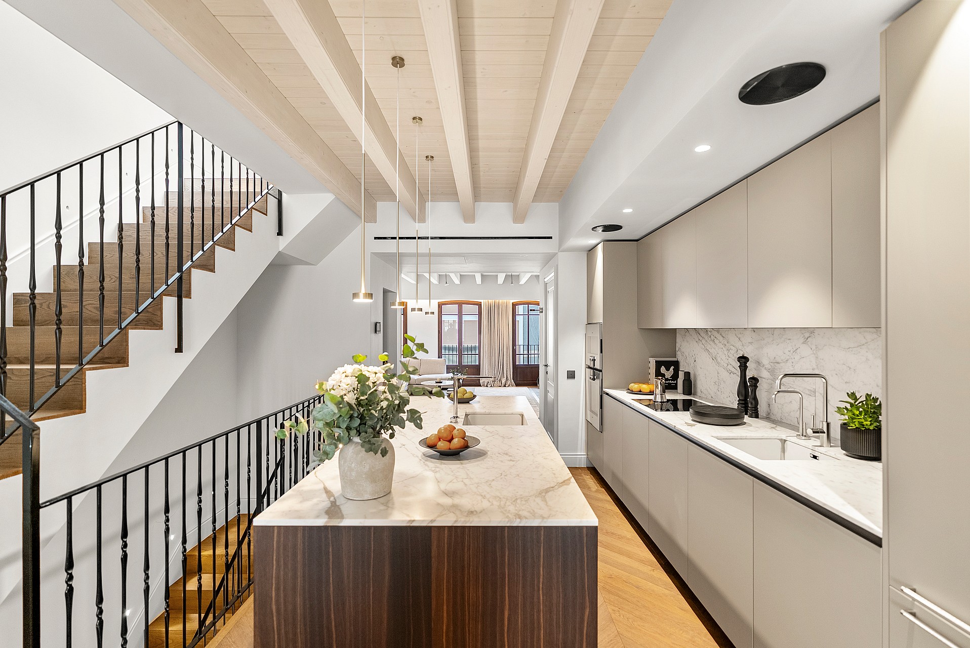 Kitchen island with marble counter and dark wood base beside a wooden staircase with black metal railings.