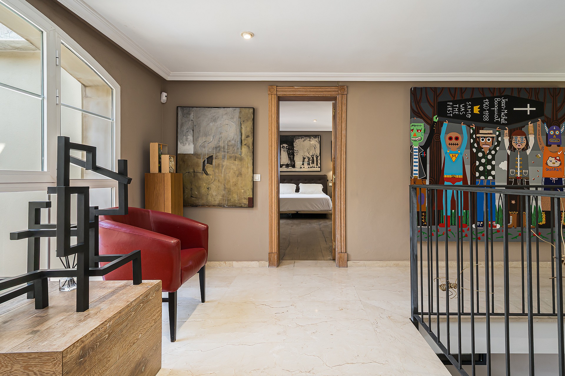 A bright mezzanine landing featuring a red leather armchair, a metal abstract sculpture, and framed wall art, overlooking the floor below.