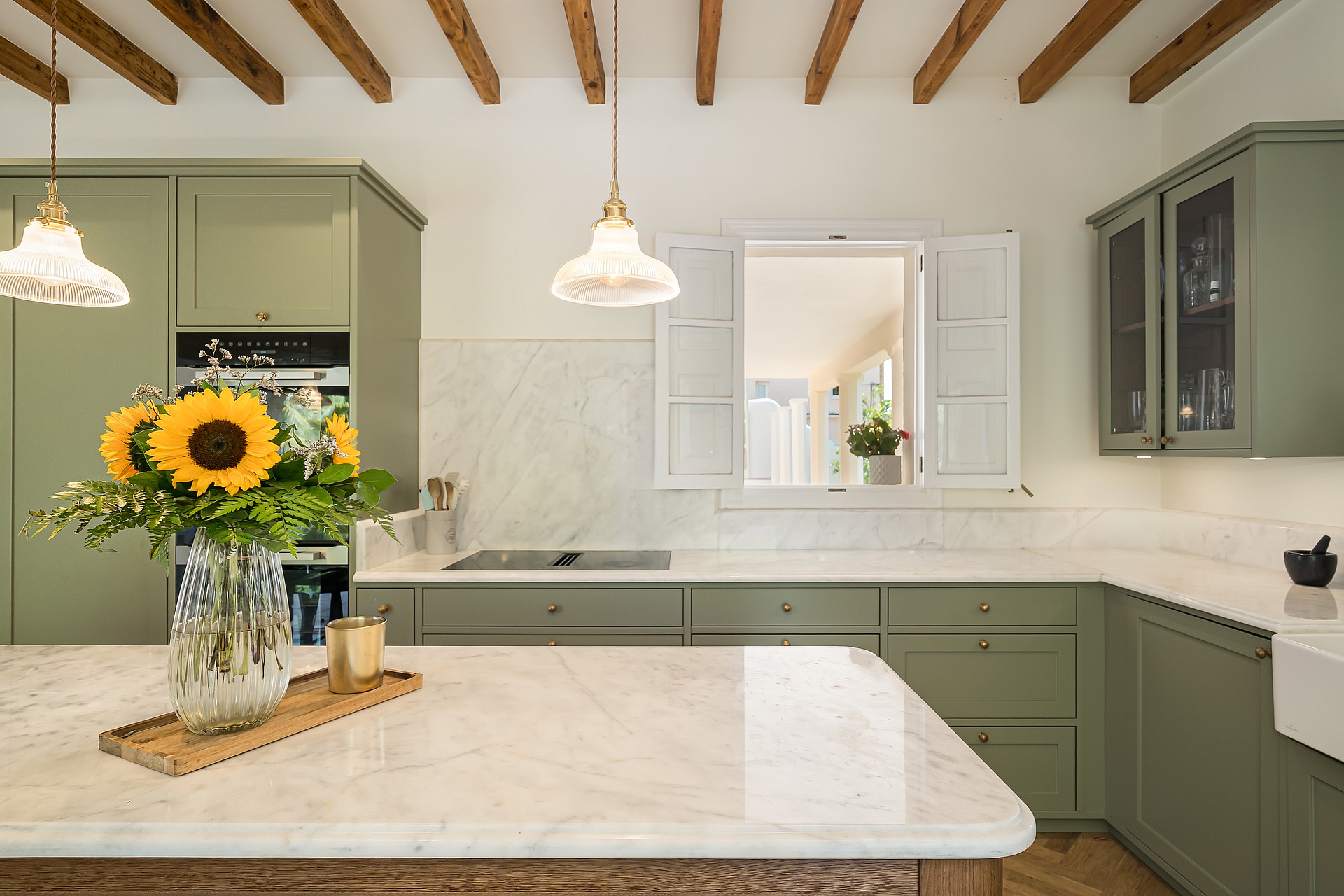 Contemporary kitchen featuring sage green cabinets, white marble countertops, exposed ceiling beams, and pendant lighting.