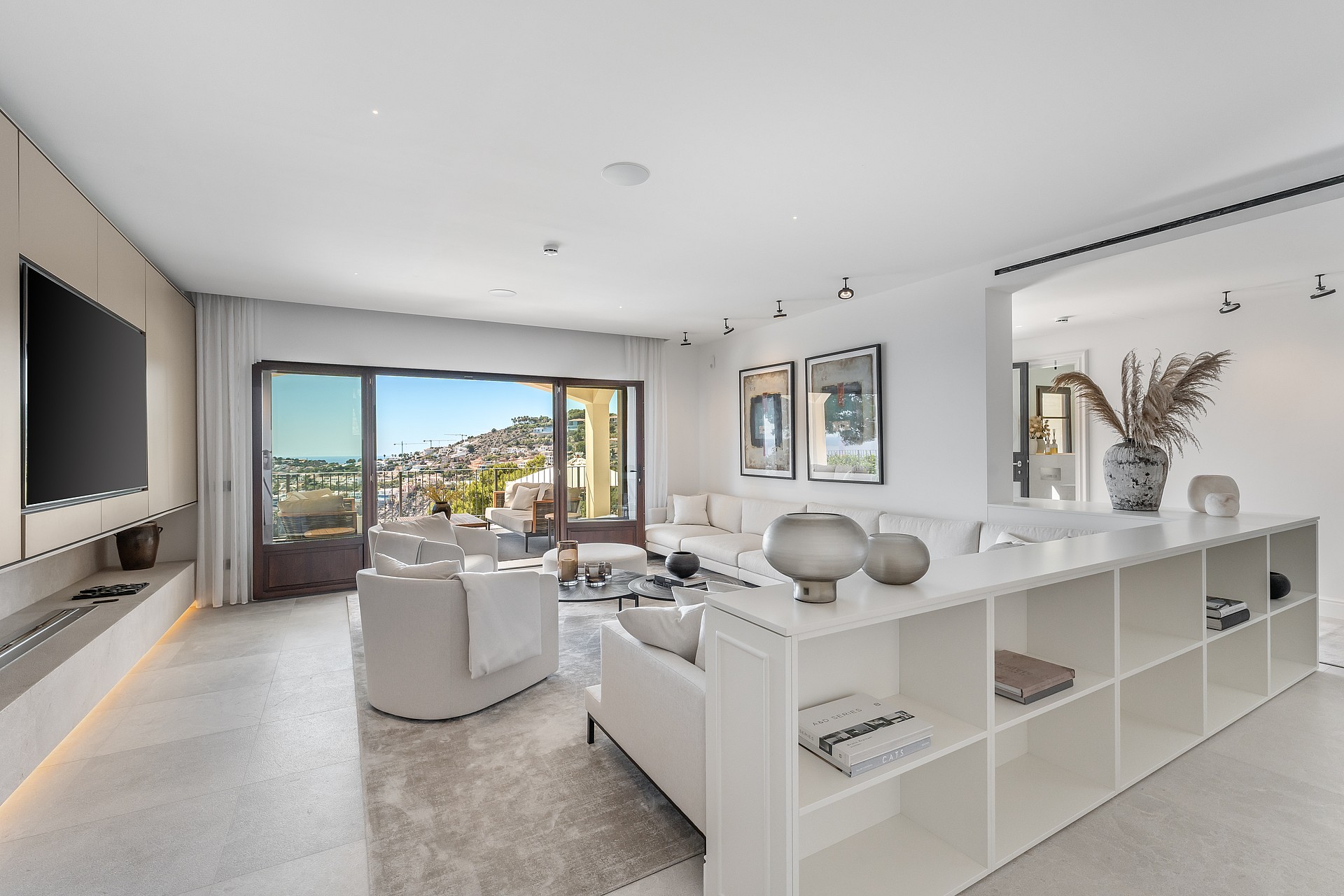 Bright living room featuring white sofas, stone floors, and large sliding doors opening to a terrace with coastal views.