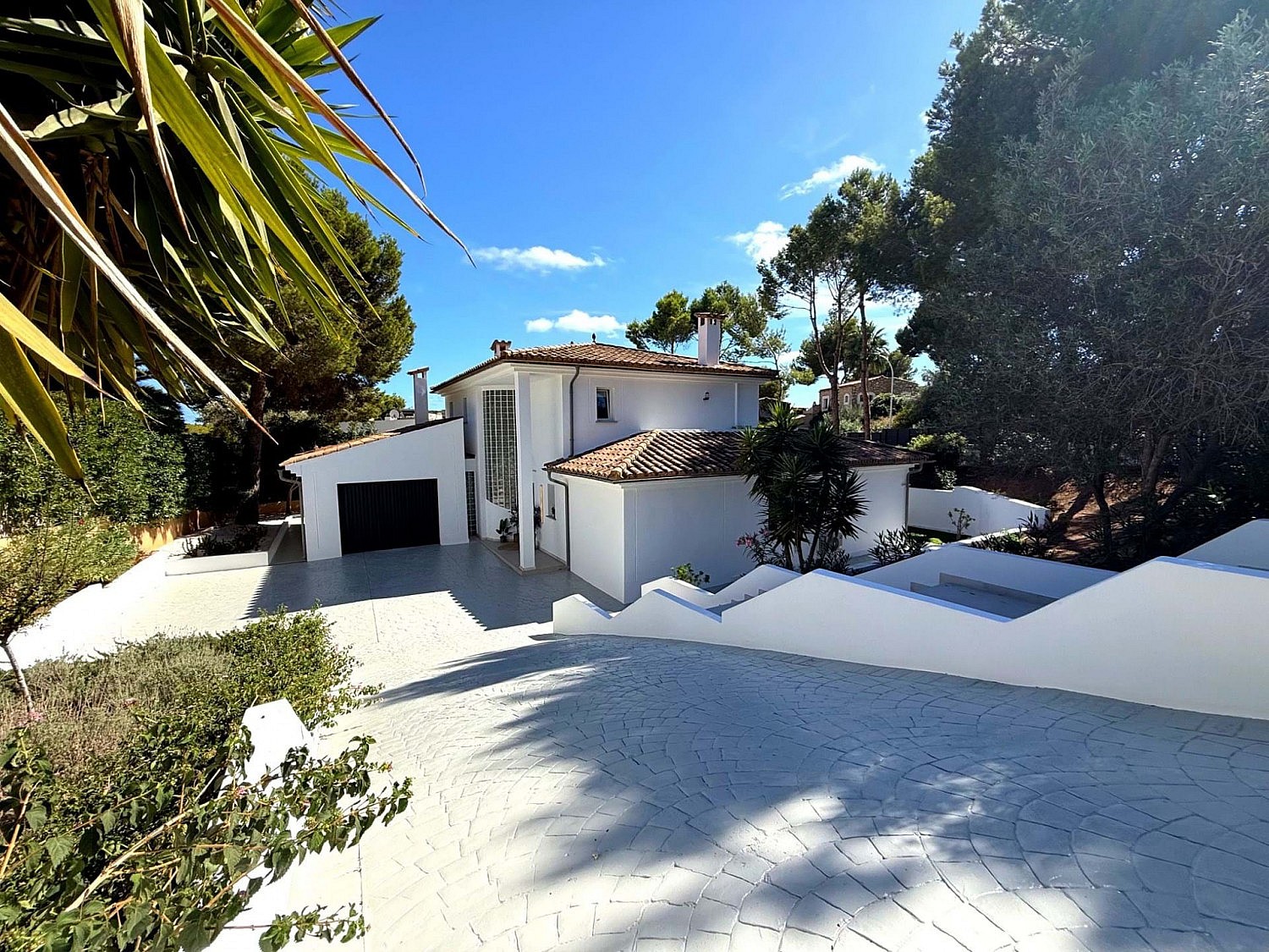 Front elevation of a white two-storey villa with terracotta roof, double garage and wide paved driveway