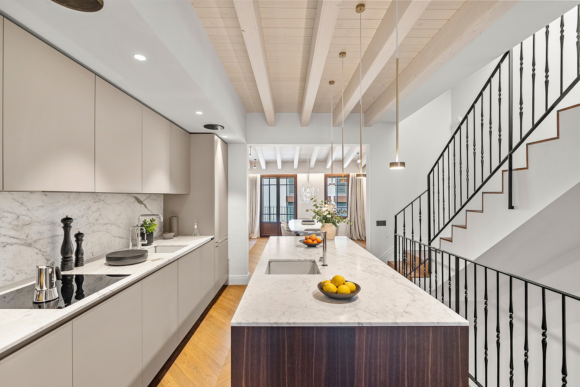 Kitchen island with marble top and dark wood base beside a staircase with black iron railings and exposed ceiling beams.