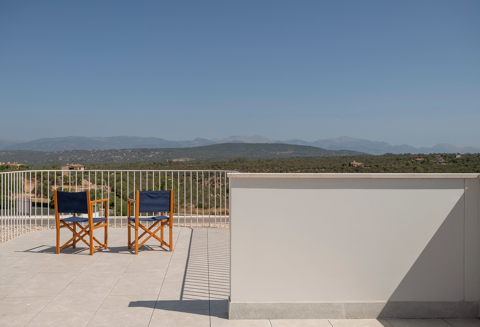Elevated stone terrace with two wooden chairs facing a mountain landscape under a clear blue sky.
