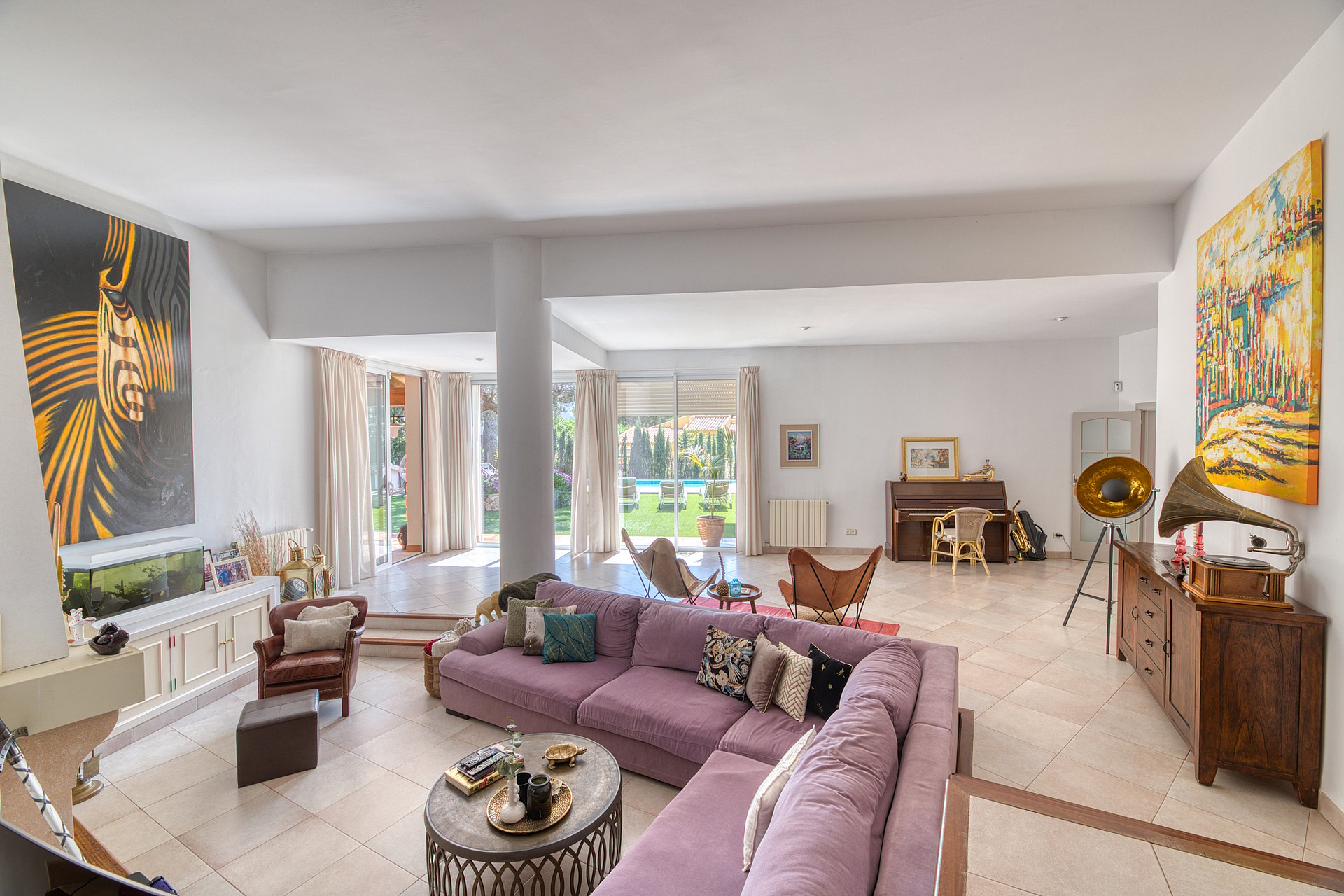 A spacious living room featuring light stone flooring, a large mauve sectional sofa, and access to a garden terrace.
