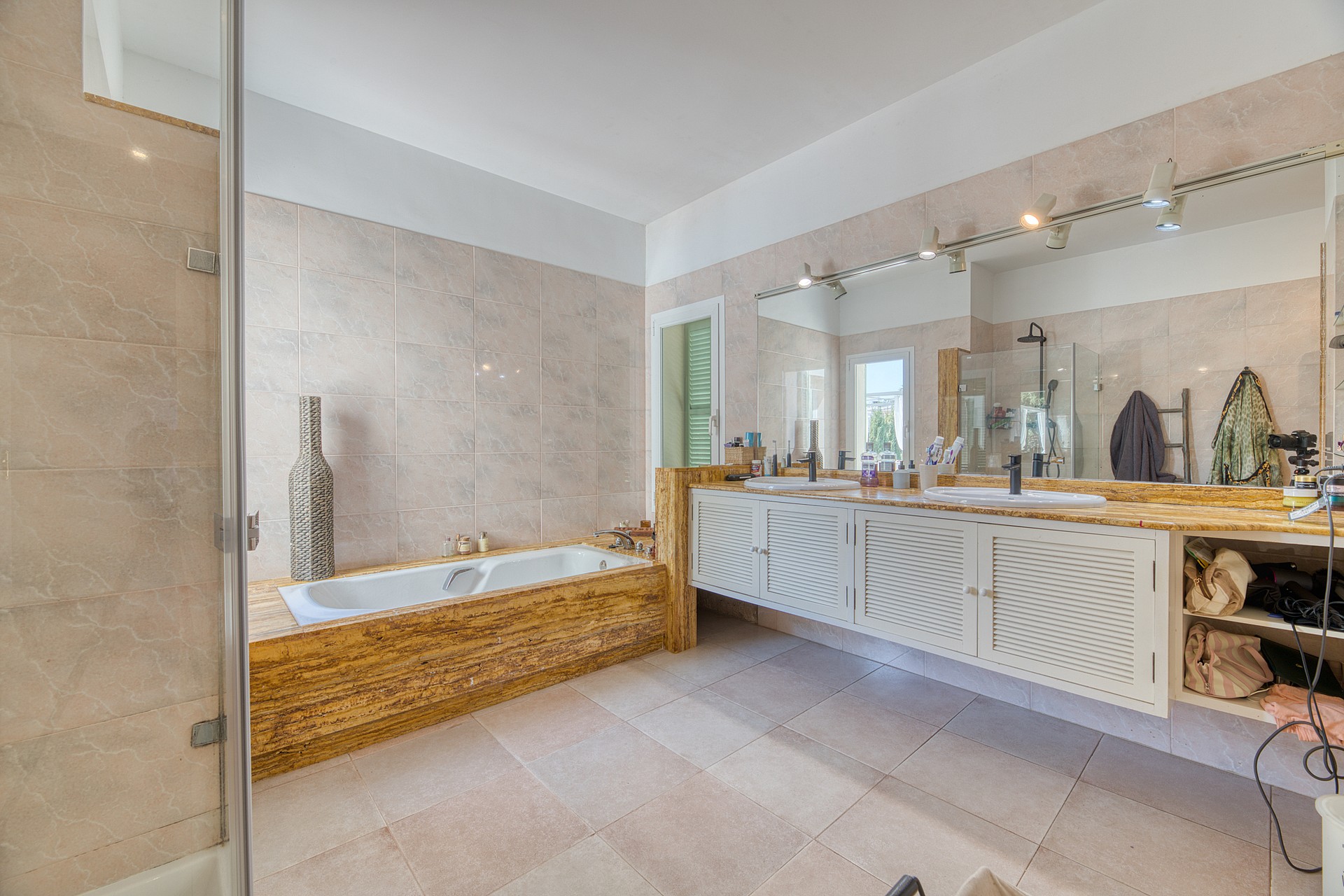 Master bathroom featuring a stone-clad soaking tub, double vanity with white cabinetry, and large wall-mounted mirrors.