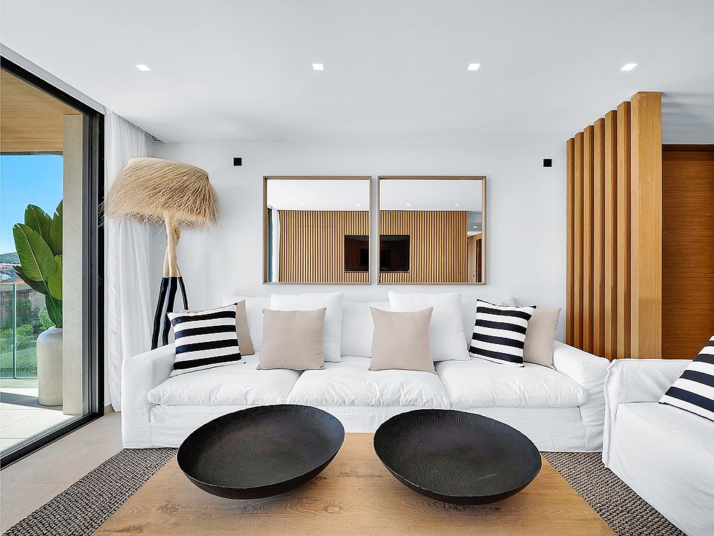 Modern living room featuring a white sofa with striped cushions, two black decorative bowls on a wooden coffee table, and vertical wood slat partitions.