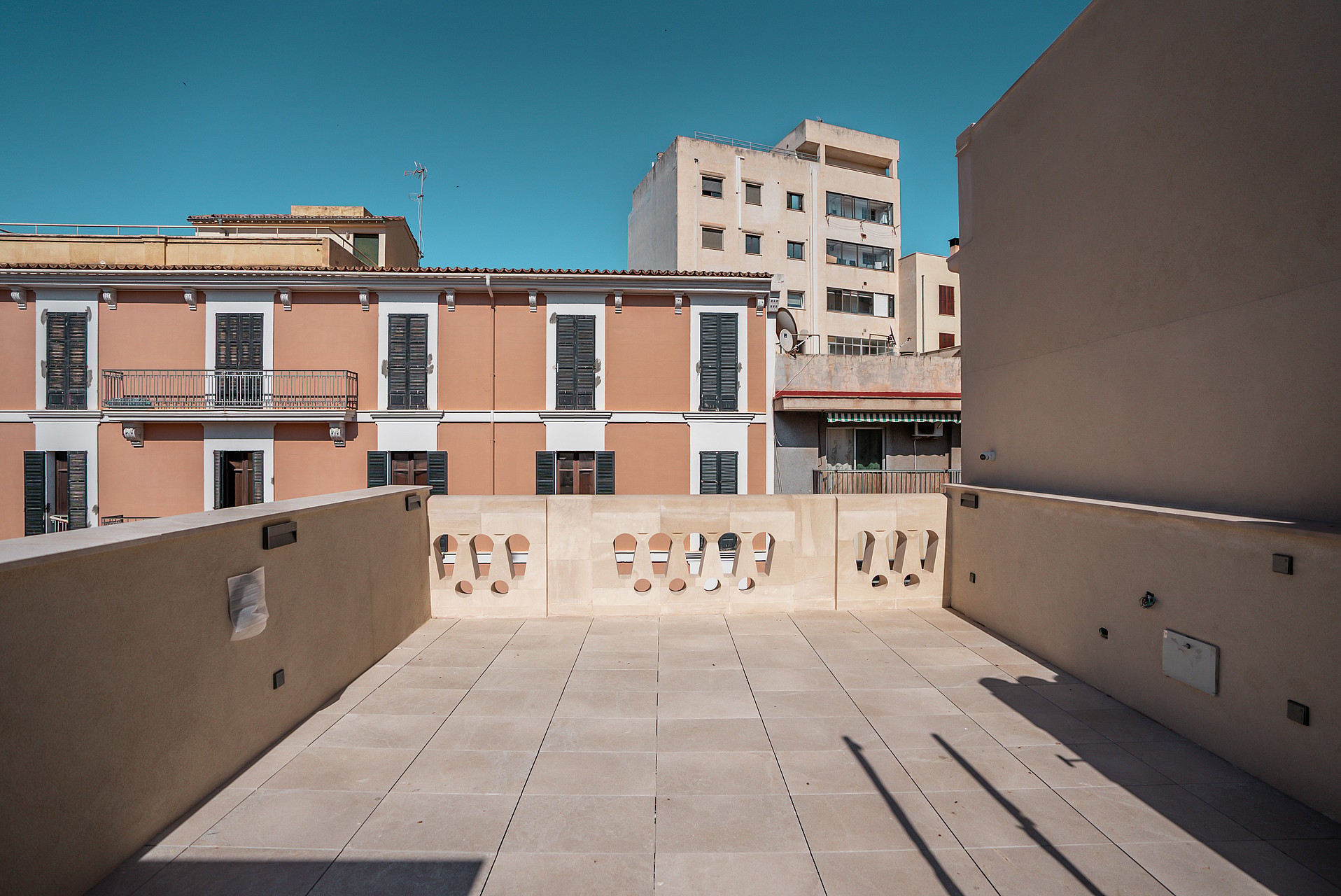 A rooftop terrace featuring square stone tiles and an ornate balustrade against a backdrop of terracotta townhouses.