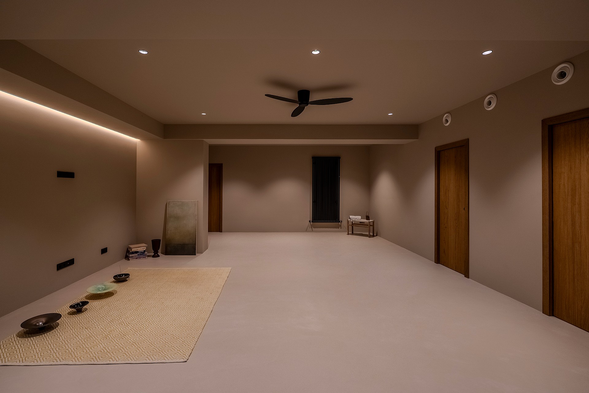 Large minimalist room with smooth beige walls, recessed ceiling lights, oak doors, and a black ceiling fan.