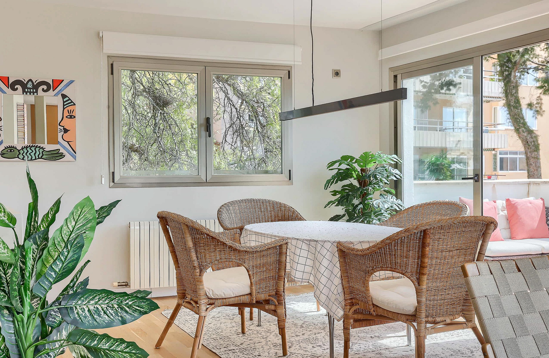 A dining space featuring four woven rattan chairs around a circular table, positioned near a window and a glass balcony door.