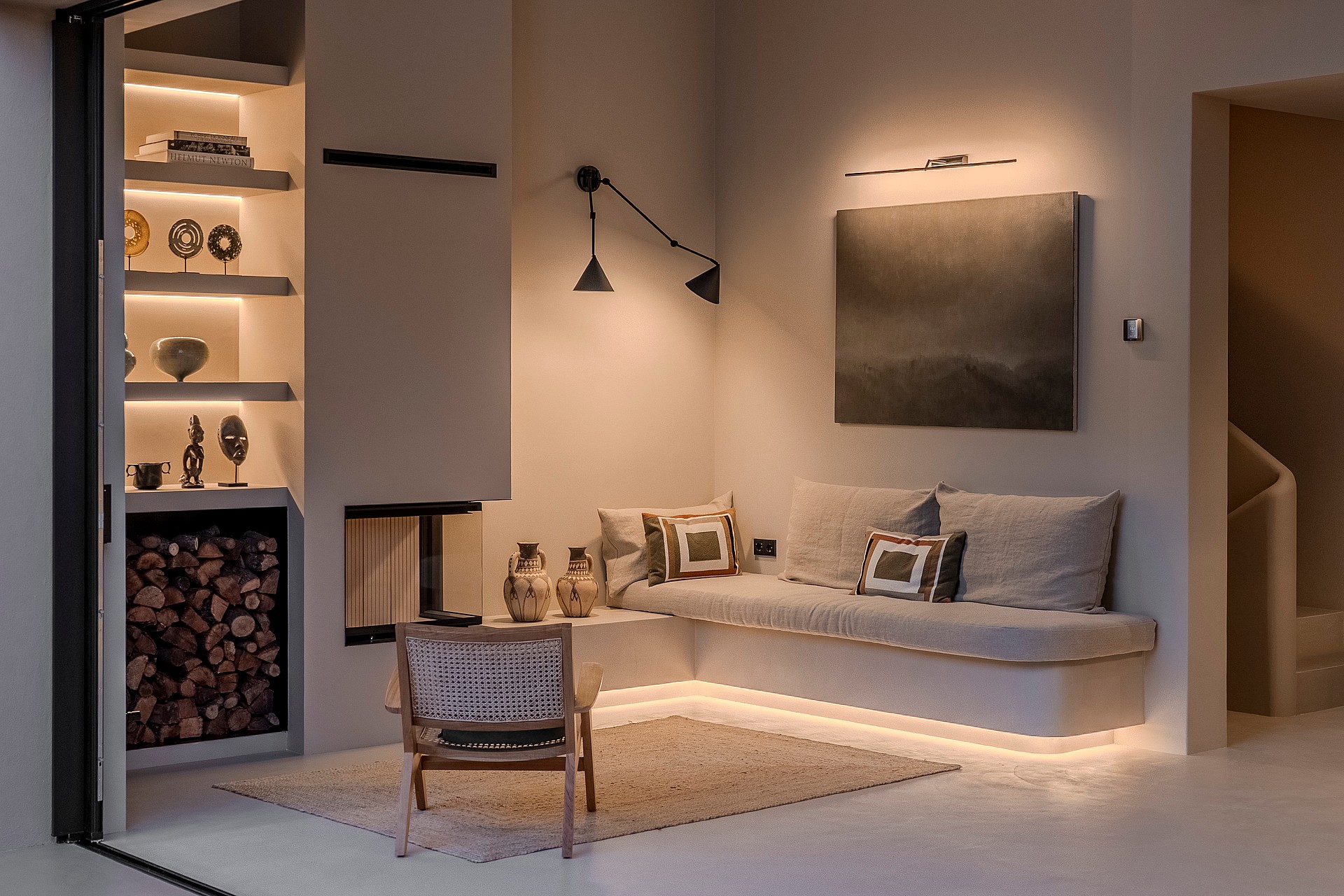 Interior view of a modern lounge featuring a glass fireplace, backlit shelving, and a floating banquette with LED lighting.