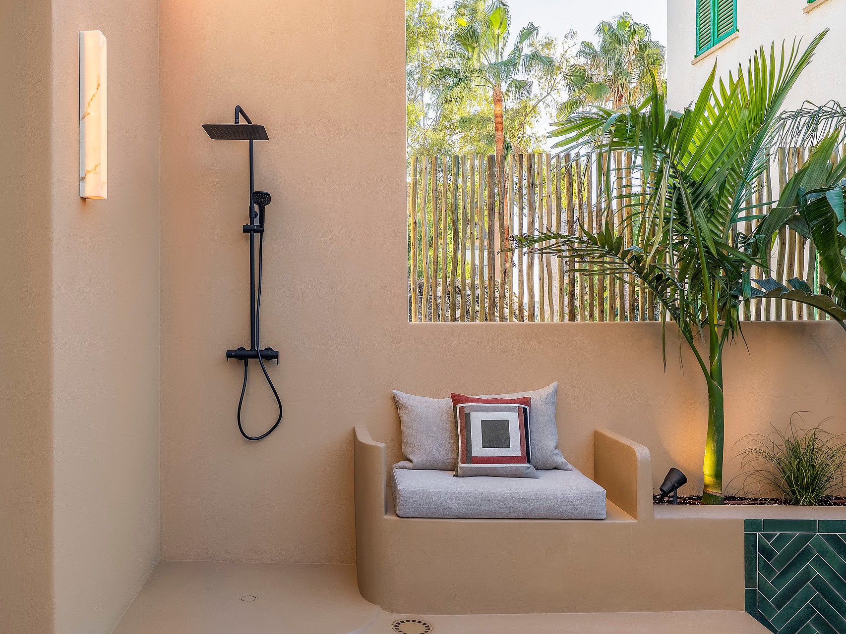 Modern outdoor shower with black fixtures next to a built-in masonry bench and tropical plants.