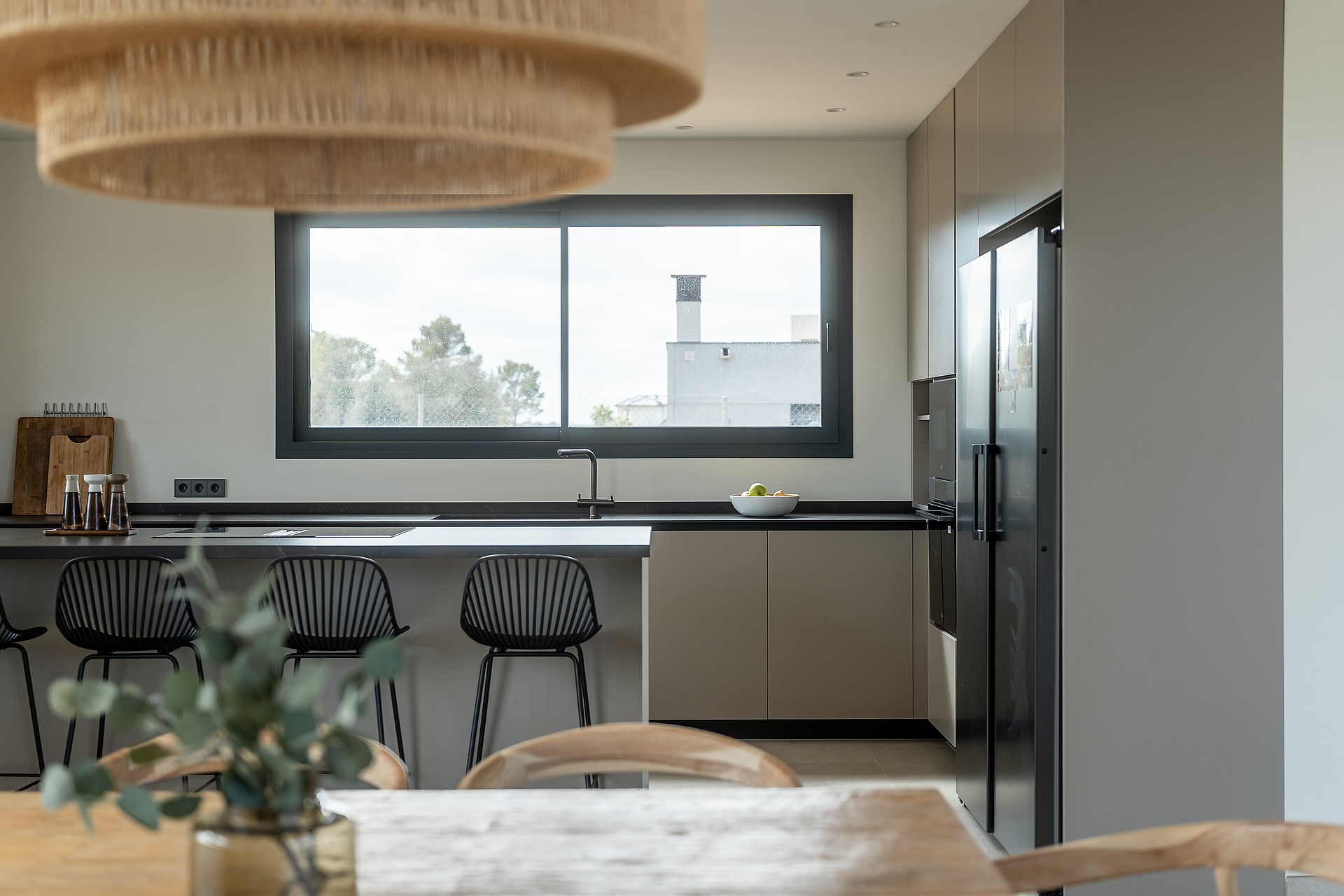 Contemporary kitchen featuring a grey island with black bar stools, dark countertops, and a wide window with mountain views.