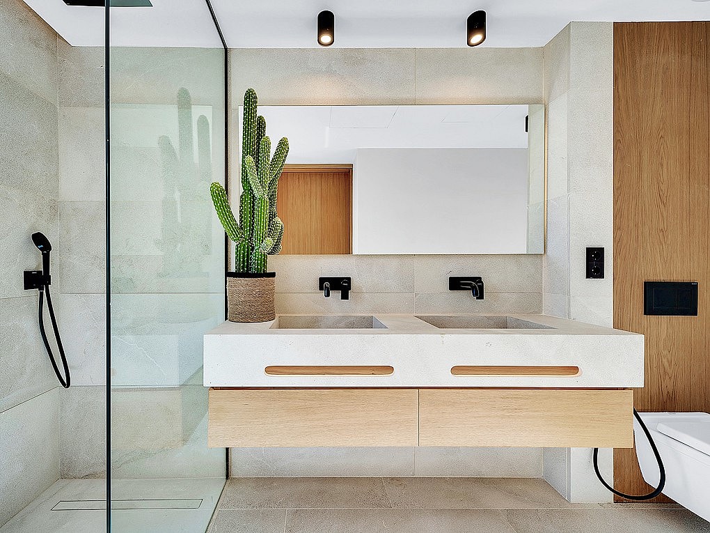 Modern bathroom featuring a floating wooden vanity, double stone sinks, black matte fixtures, and a glass-enclosed shower.