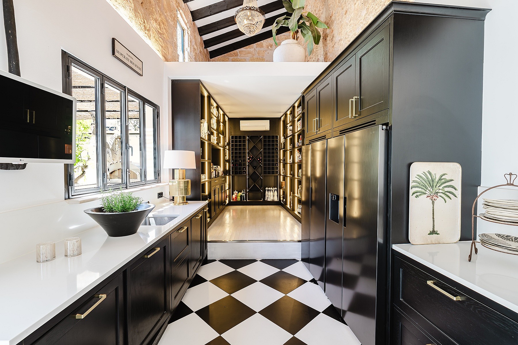 A modern kitchen with black cabinetry, white countertops, and a black-and-white checkered floor leading into a back pantry.